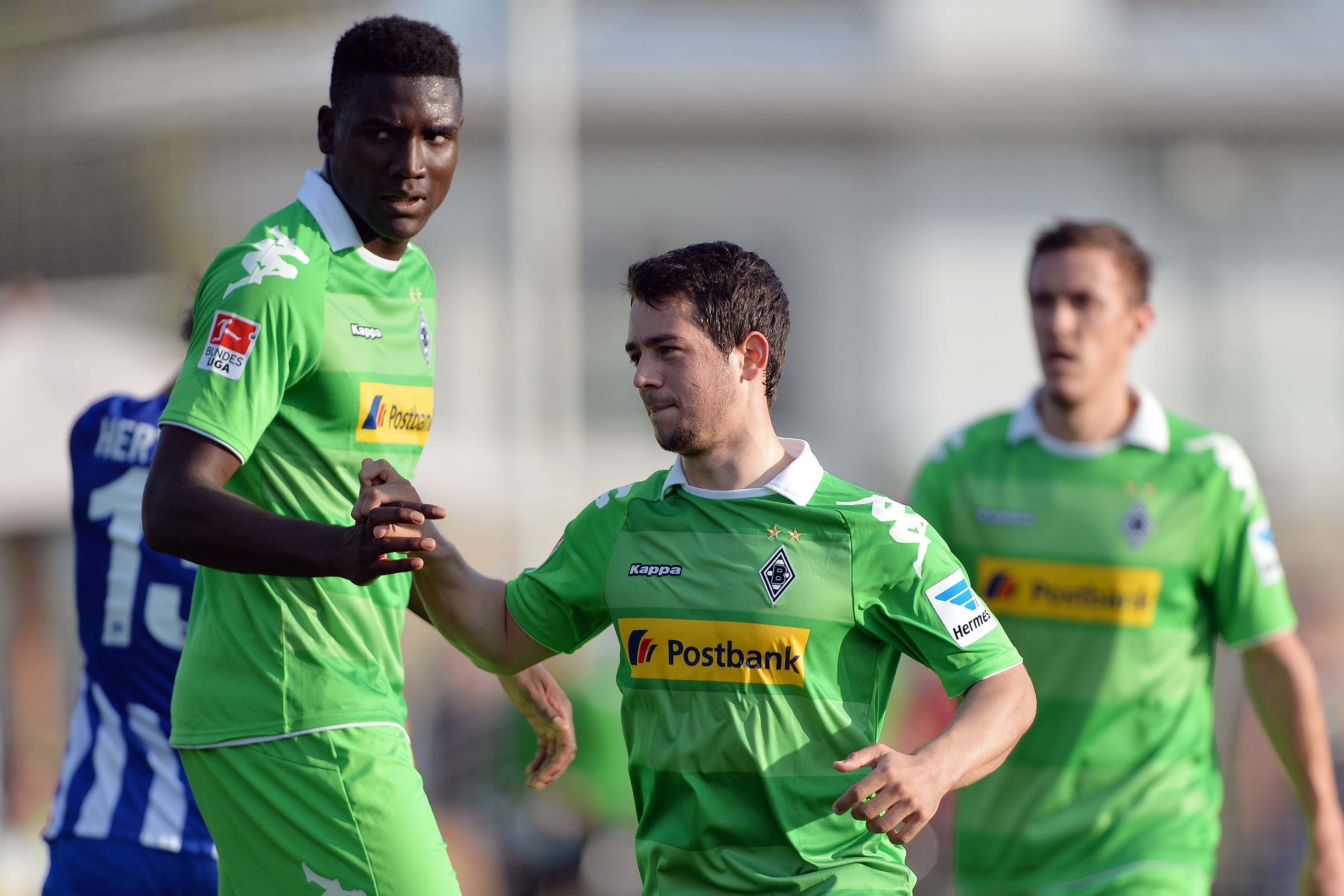 Peniel Mlapa und Amin Younes schlagen in einem Testspiel von Borussia Mönchengladbach gegen Hertha BSC am 15. Januar 2014 ein. Im Hintergrund joggt Max Kruse heran. Die Borussia-Spieler tragen ein knallgrünes Trikot.