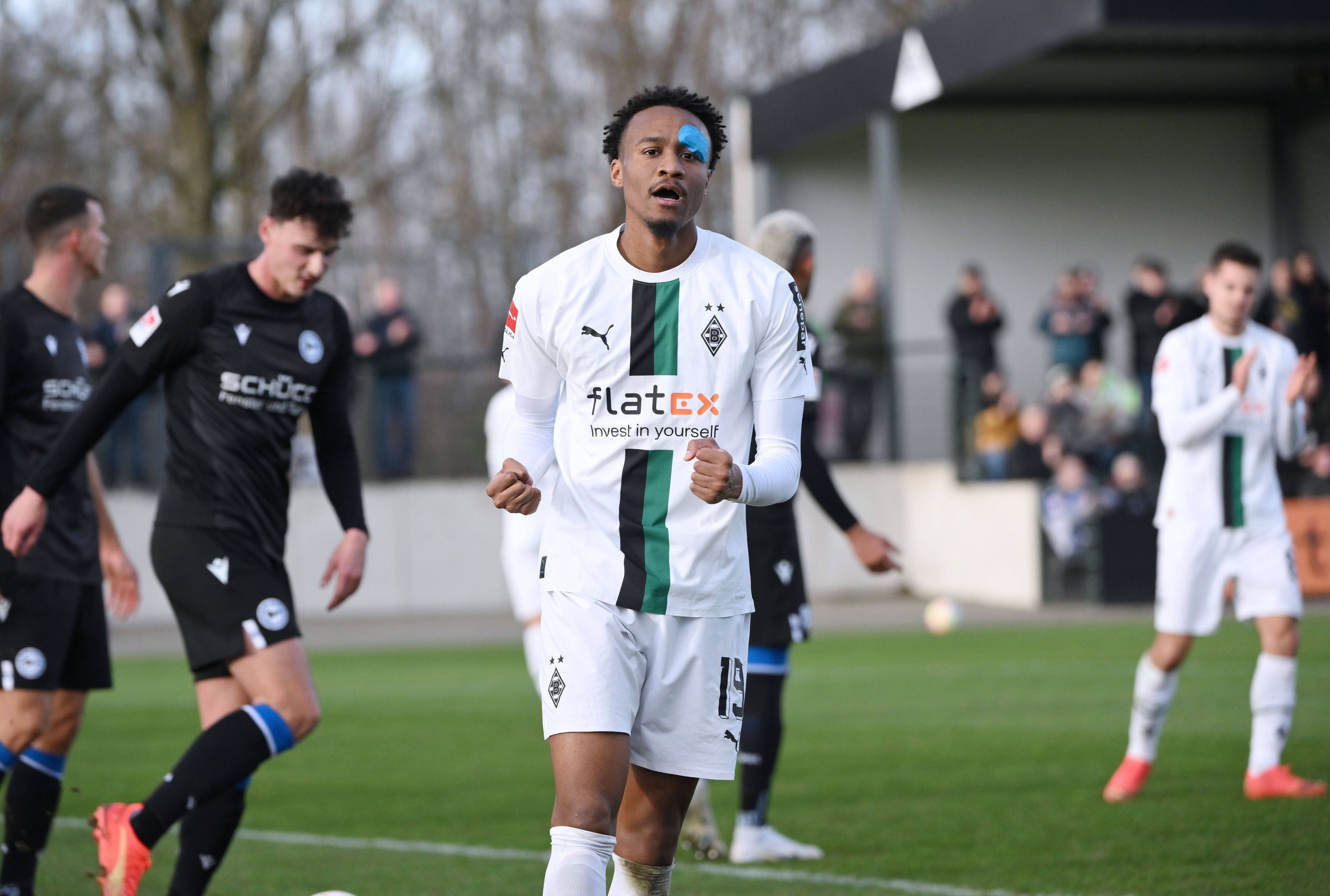 Nathan Ngoumou streckt die Arme nach oben und ballt bei seinem Jubel die Fäuste, nachdem er das 1:0 für Borussia Mönchengladbach im Testspiel gegen Arminia Bielefeld am 11. Januar 2023 erzielt hat. Ngoumou trägt das weiße Heimtrikot von Borussia und nach einer Augen-Infektion einen blauen Tape-Verband im Gesicht.
