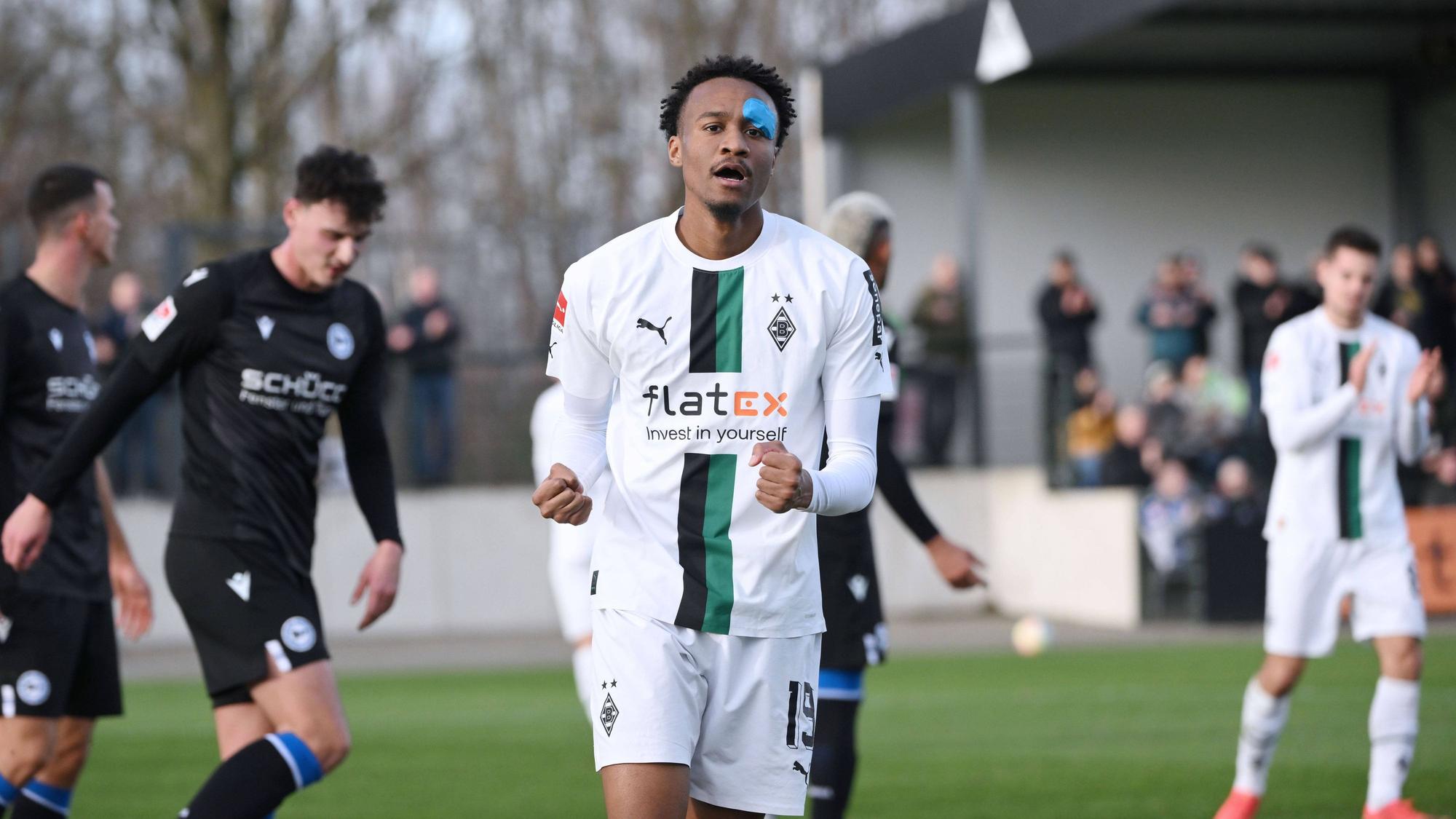 Nathan Ngoumou streckt die Arme nach oben und ballt bei seinem Jubel die Fäuste, nachdem er das 1:0 für Borussia Mönchengladbach im Testspiel gegen Arminia Bielefeld am 11. Januar 2023 erzielt hat. Ngoumou trägt das weiße Heimtrikot von Borussia und nach einer Augen-Infektion einen blauen Tape-Verband im Gesicht.