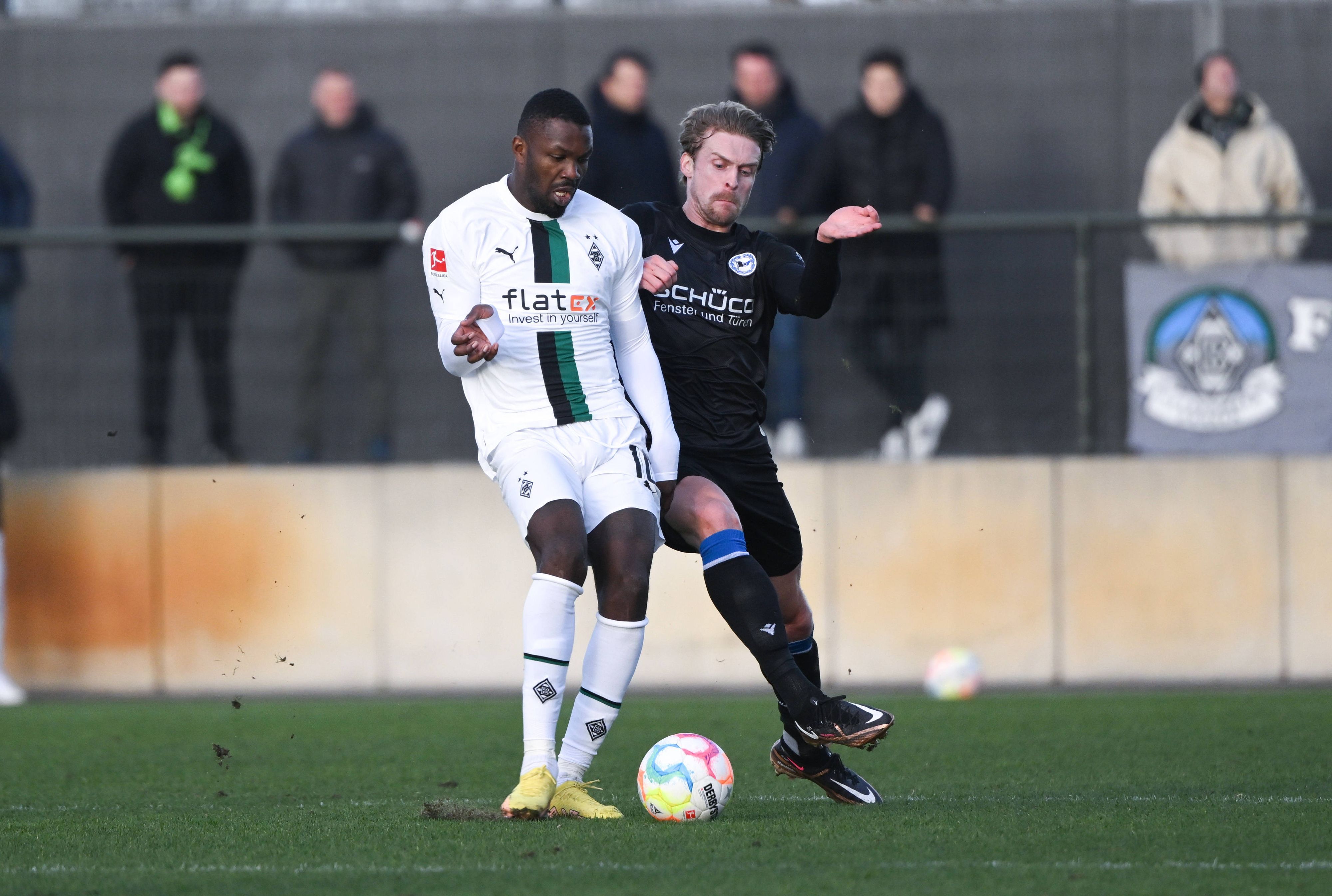 Marcus Thuram bereitet sich beim Testspiel von Borussia Mönchengladbach gegen Arminia Bielefeld am 11. Januar 2023 auf dem Fohlenplatz auf einen Schuss mit dem rechten Fuß vor, Bielefeld-Verteidiger Oliver Husing will ihn noch stoppen. Thuram trägt das weiße Borussia-Heimtrikot.