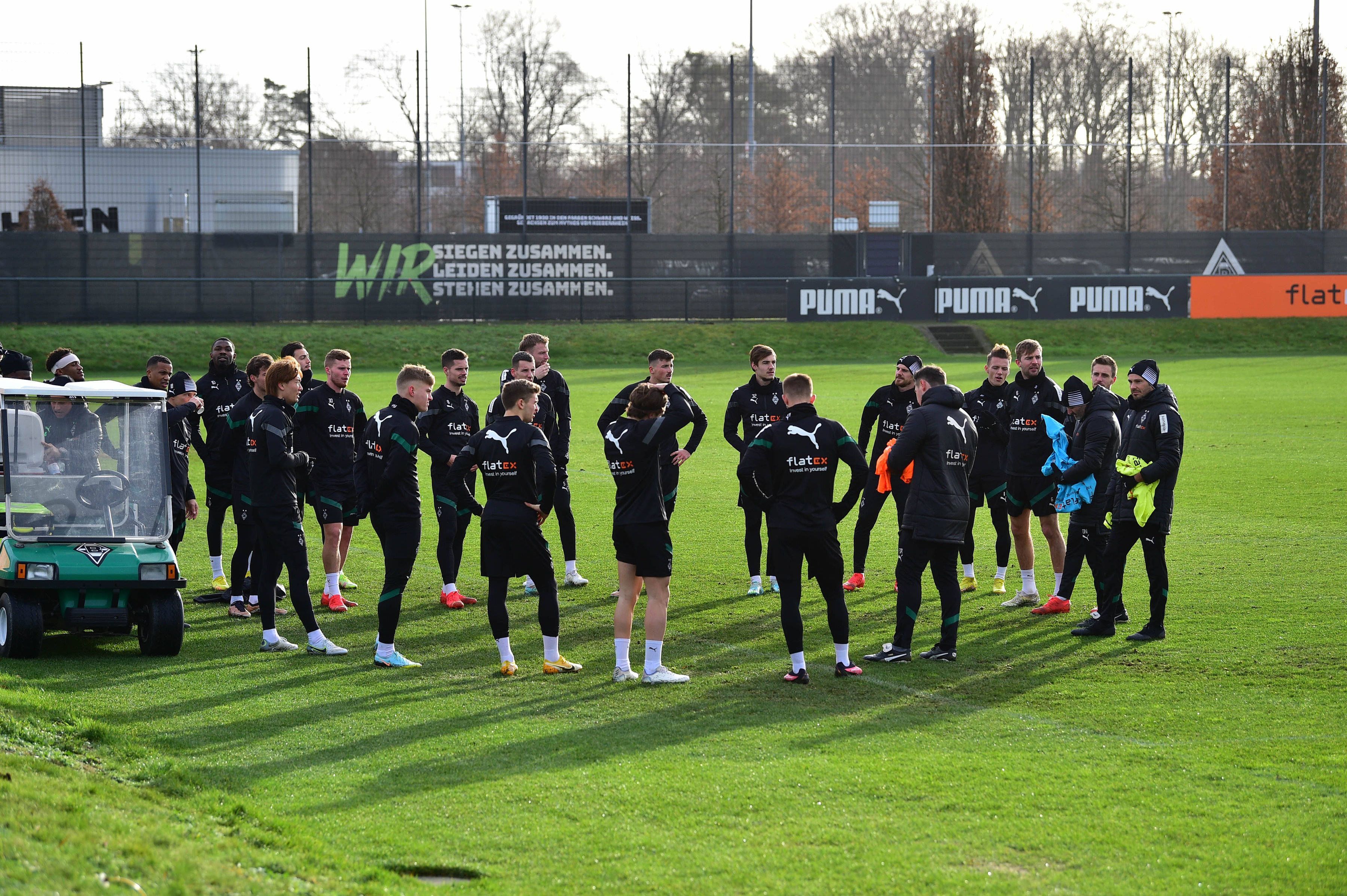 Die Spieler von Borussia Mönchengladbach und einige Mitglieder des Trainerstabs stehen im Rahmen einer Trainingseinheit auf dem Trainingsplatz im Borussia-Park im Kreis. Alle Spieler tragen dabei dunkle Borussia-Trainingskleidung, aufgenommen wurde das Foto am 10. Januar 2023.