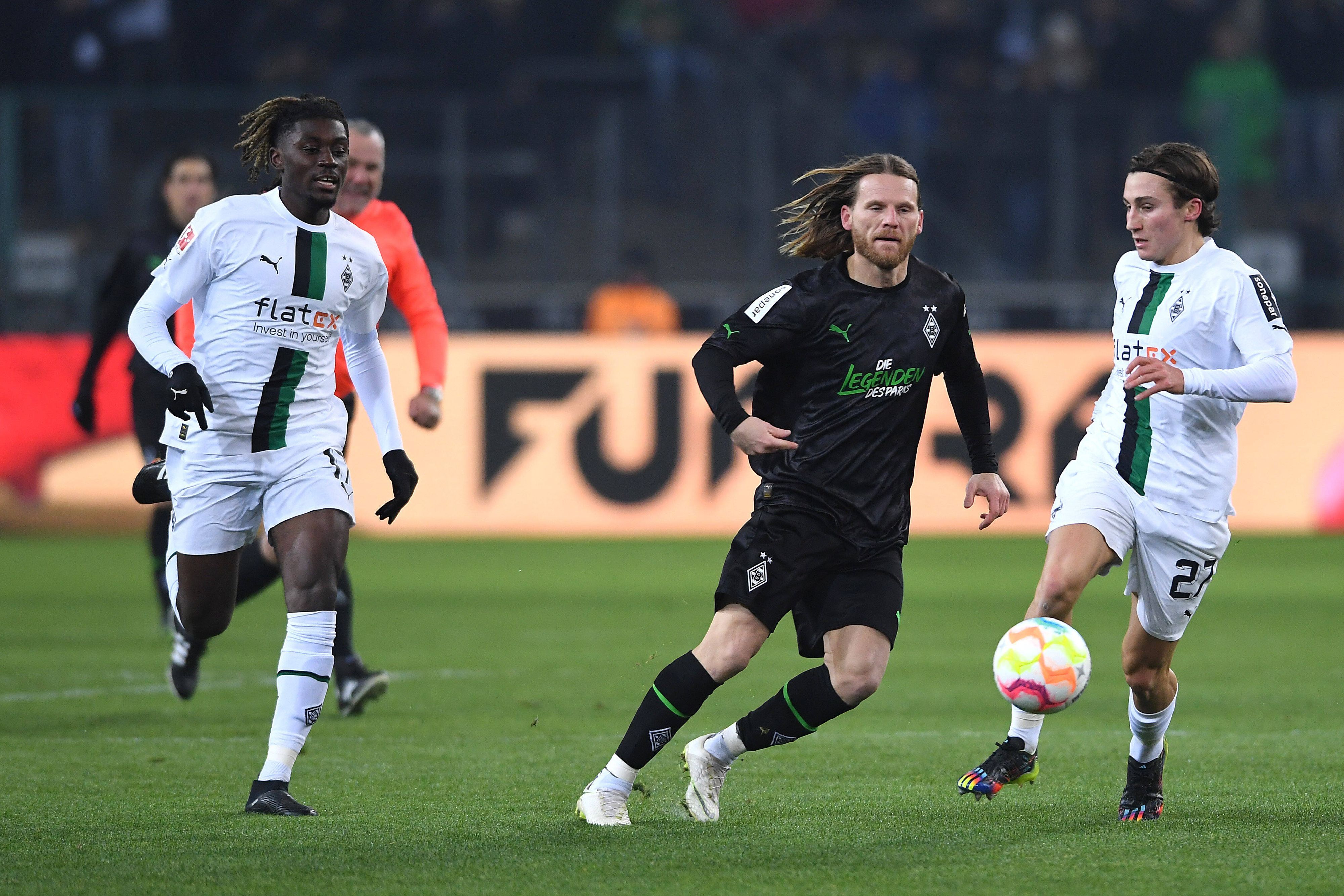 Rocco Reitz (r.) und Manu Koné (l.) treiben den Ball im weißen Heimtrikot von Borussia Mönchengladbach beim Legendenspiel am 17. Dezember 2022 nach vorne. Angegriffen wird Reitz von U23-Trainer Eugen Polanski (M.) im schwarzen Trikot der Borussia-Legenden.