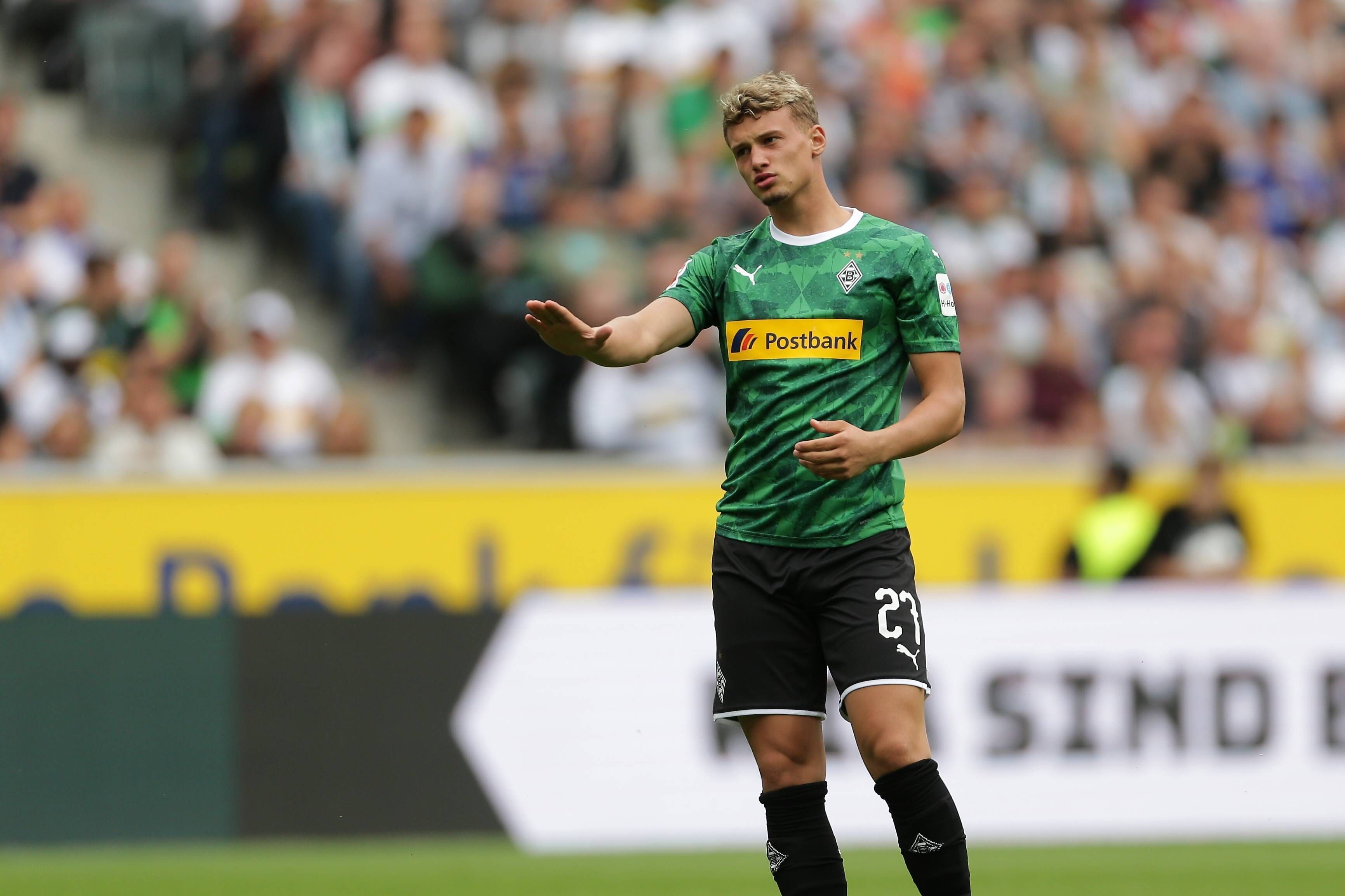 Michael Cuisance im Trikot von Borussia Mönchengladbach am 3. August 2019. Der Mittelfeldspieler aus Frankreich trägt ein grünes Gladbach-Trikot und macht eine beruhigende Geste mit seinem rechten Arm.