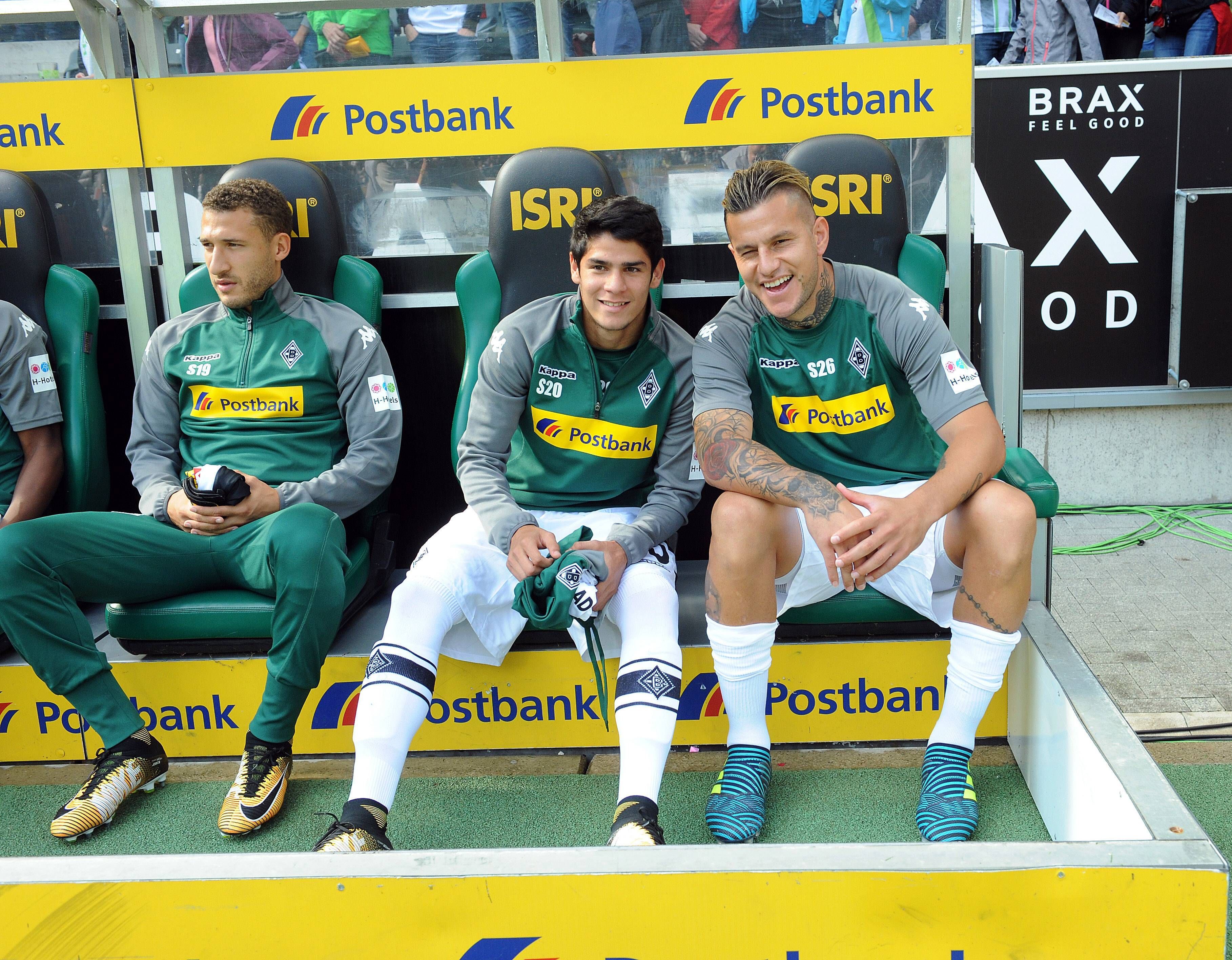 Julio Villalba (M.) sitzt am 9. September 2017 auf der Bank im Borussia-Park zwischen Fabian Johnson (l.) und Raul Bobadilla (r.). Villalba hält ein Trikot von Borussia in der Hand.