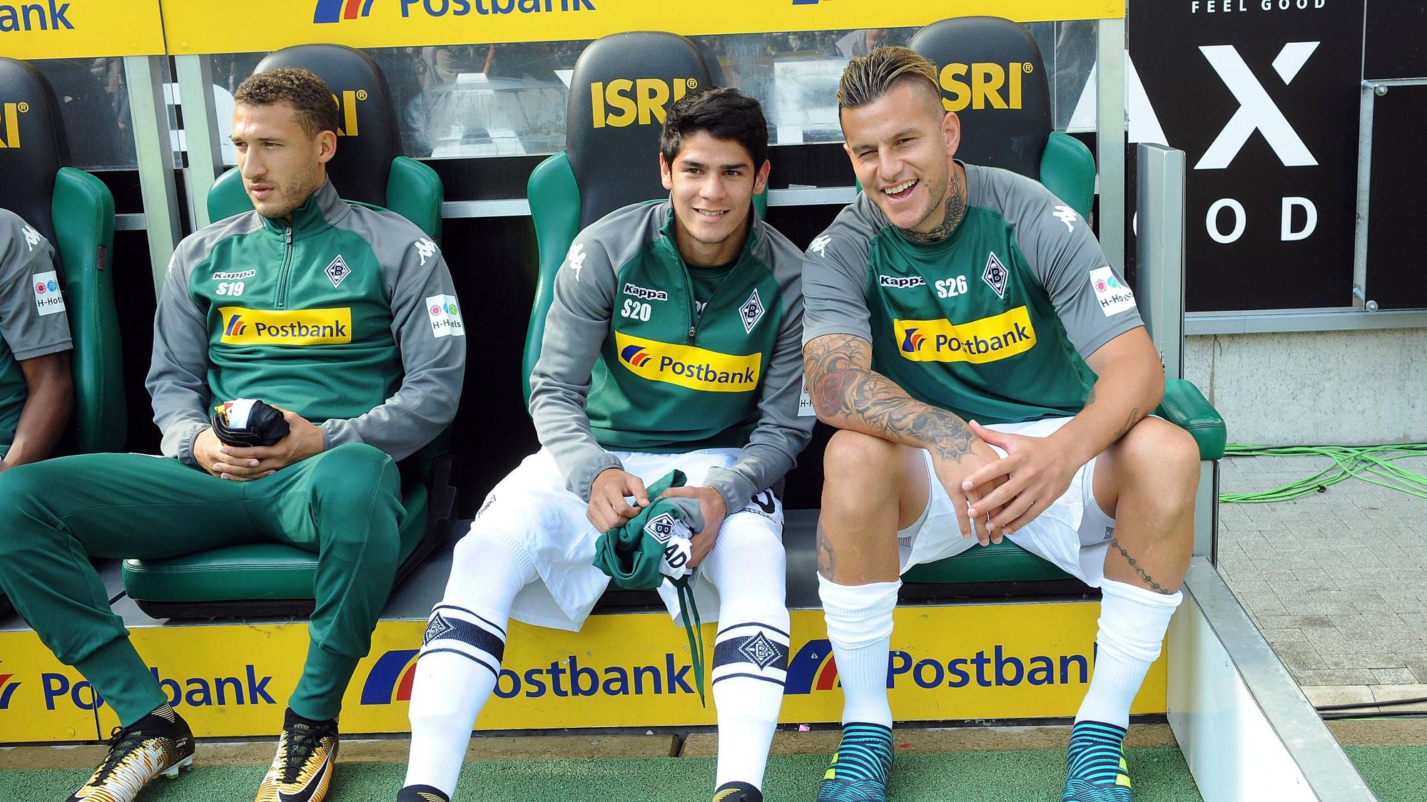 Julio Villalba (M.) sitzt am 9. September 2017 auf der Bank im Borussia-Park zwischen Fabian Johnson (l.) und Raul Bobadilla (r.). Villalba hält ein Trikot von Borussia in der Hand.