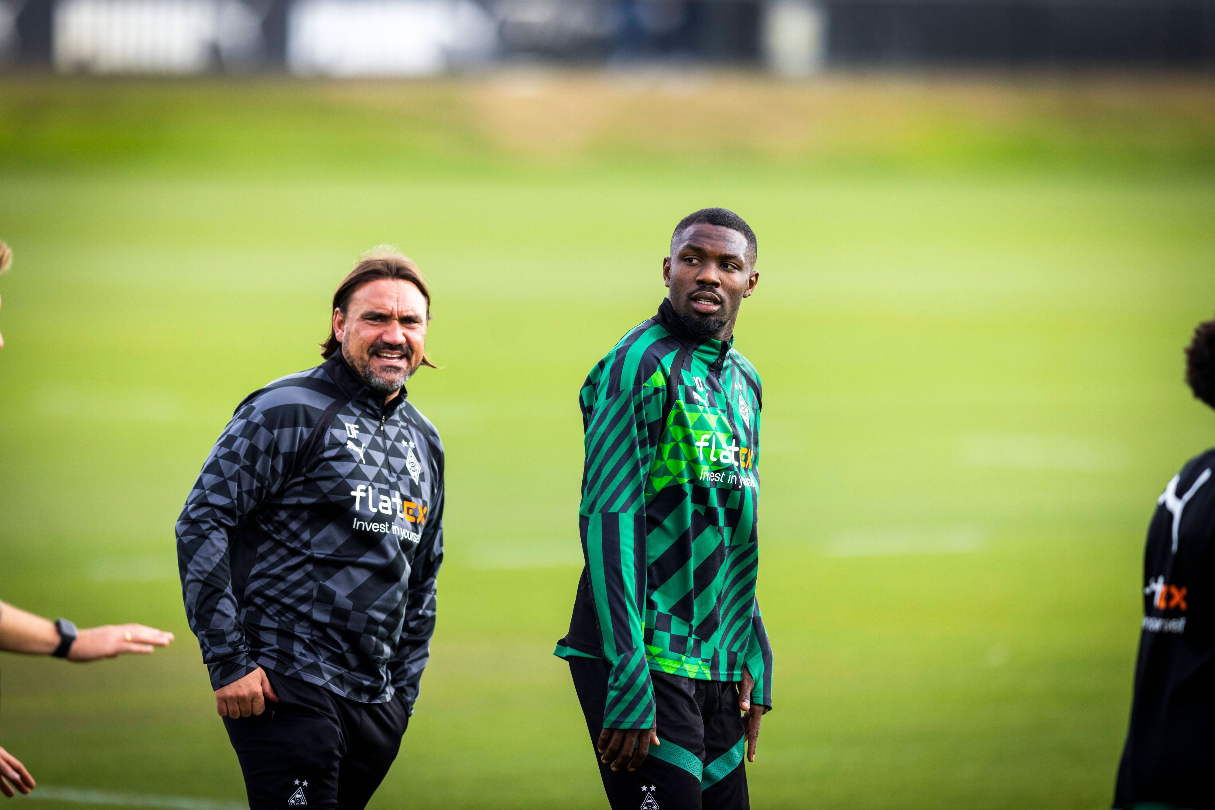 Daniel Farke (l.), Trainer von Borussia Mönchengladbach, und Marcus Thuram stehen auf dem Trainingsplatz im Borussia-Park nebeneinander. Farke und Thuram tragen Gladbach-Trainingskleidung.