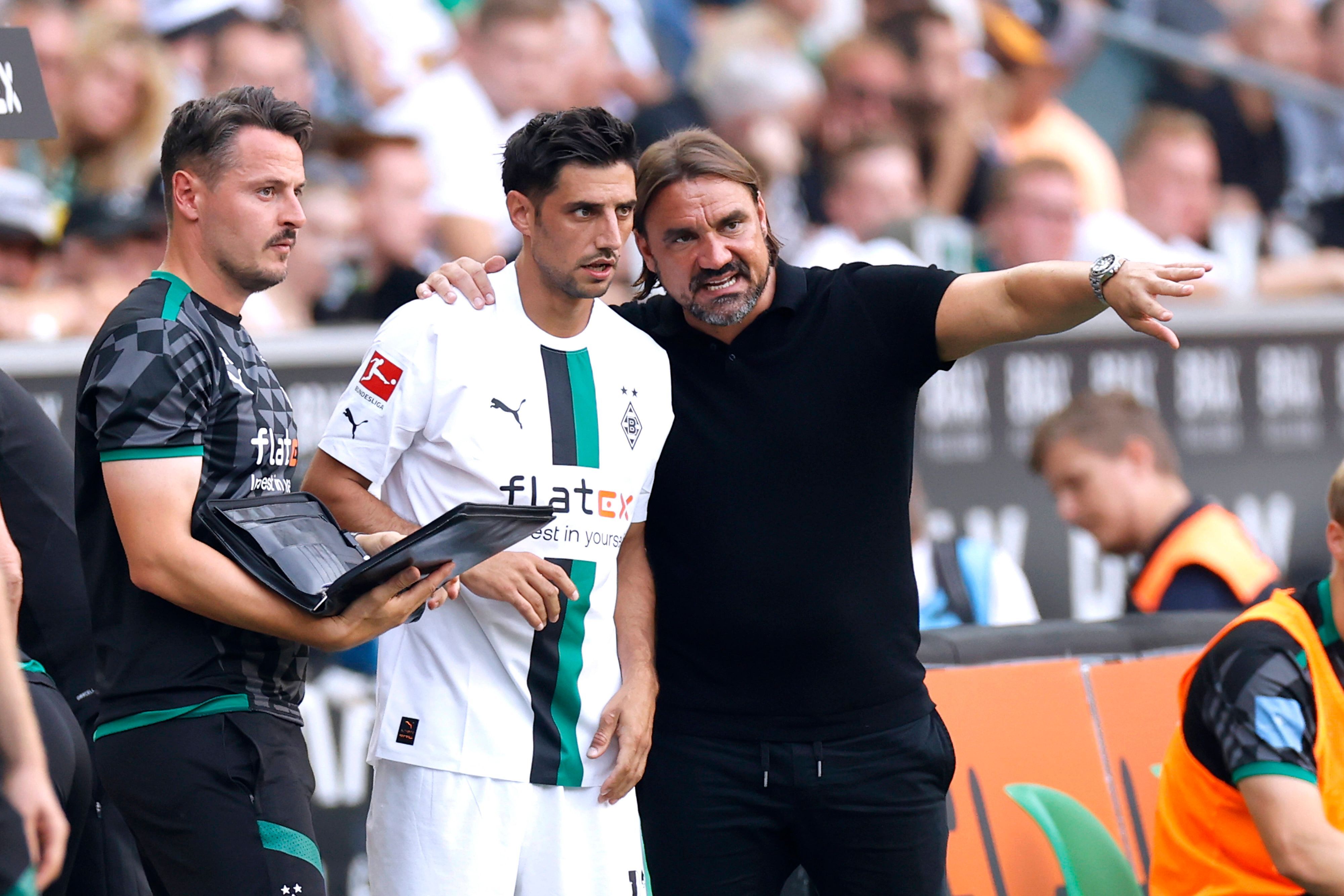 Daniel Farke (r.) legt seinen Arm um Lars Stindl (M.) und gibt dem Kapitän von Borussia Mönchengladbach vor einer Einwechslung taktische Anweisungen. Farke macht zudem eine Geste mit seinem linken Arm. Neben Farke und Stindl steht Co-Trainer Edmund Riemer und hält eine Mappe in der Hand.