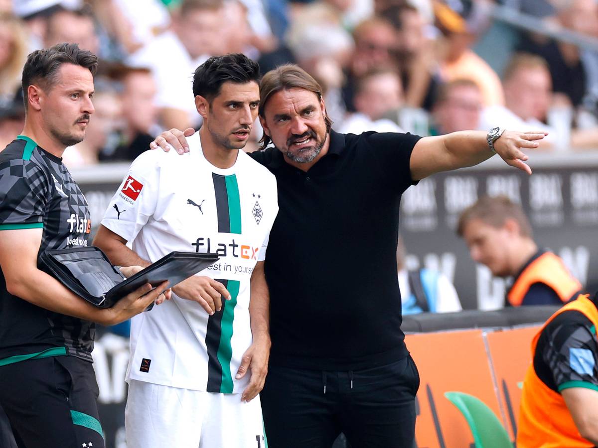 Daniel Farke (r.) legt seinen Arm um Lars Stindl (M.) und gibt dem Kapitän von Borussia Mönchengladbach vor einer Einwechslung taktische Anweisungen. Farke macht zudem eine Geste mit seinem linken Arm. Neben Farke und Stindl steht Co-Trainer Edmund Riemer und hält eine Mappe in der Hand.