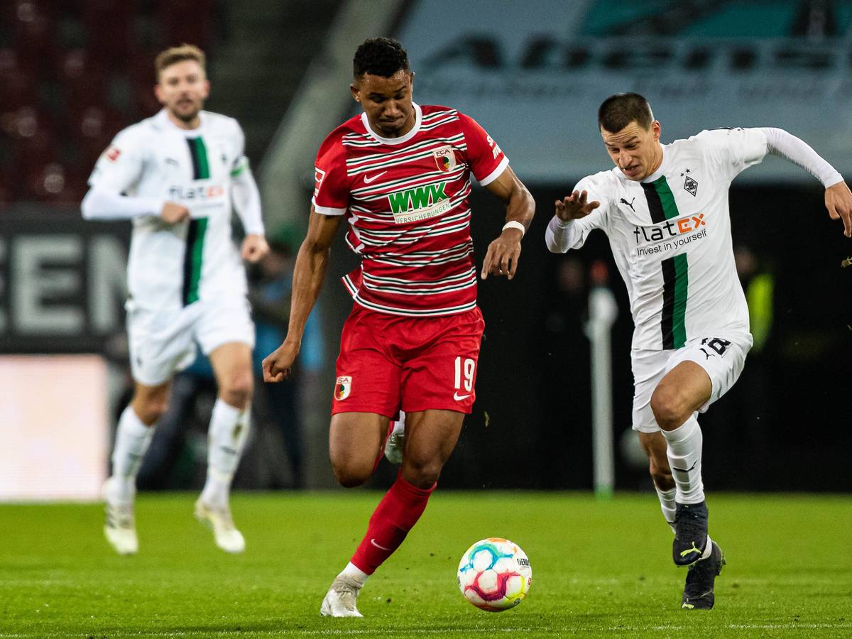 Gladbach-Verteidiger Stefan Lainer (r.) im Duell mit Felix Uduokhai (l.) vom FC Augsburg während des Bundesliga-Duells am Mittwoch (25. Januar 2023) in der WWK-Arena. Beide Spieler haben den Ball im Blick und sprinten.