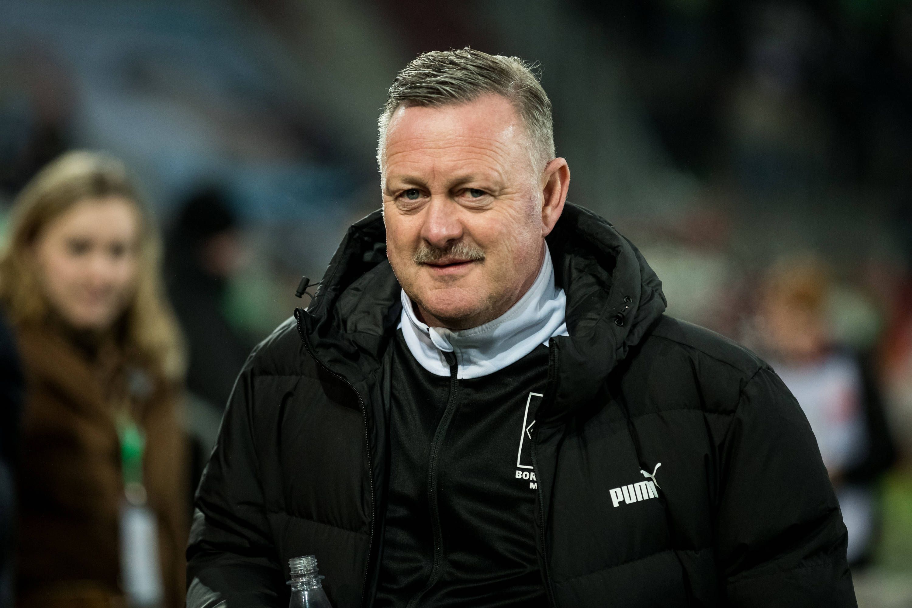 Roland Virkus steht am Spielfeldrand der WWK-Arena in Augsburg im Rahmen des Bundesliga-Spiels FC Augsburg gegen Borussia Mönchengladbach am 25. Januar 2023. Der Sportdirektor von Borussia Mönchengladbach trägt eine Winterjacke von Gladbach-Ausrüster Puma.