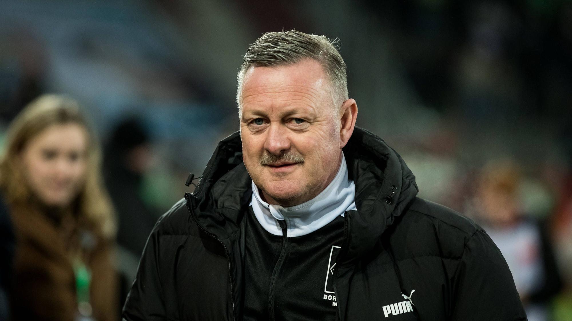 Roland Virkus steht am Spielfeldrand der WWK-Arena in Augsburg im Rahmen des Bundesliga-Spiels FC Augsburg gegen Borussia Mönchengladbach am 25. Januar 2023. Der Sportdirektor von Borussia Mönchengladbach trägt eine Winterjacke von Gladbach-Ausrüster Puma.