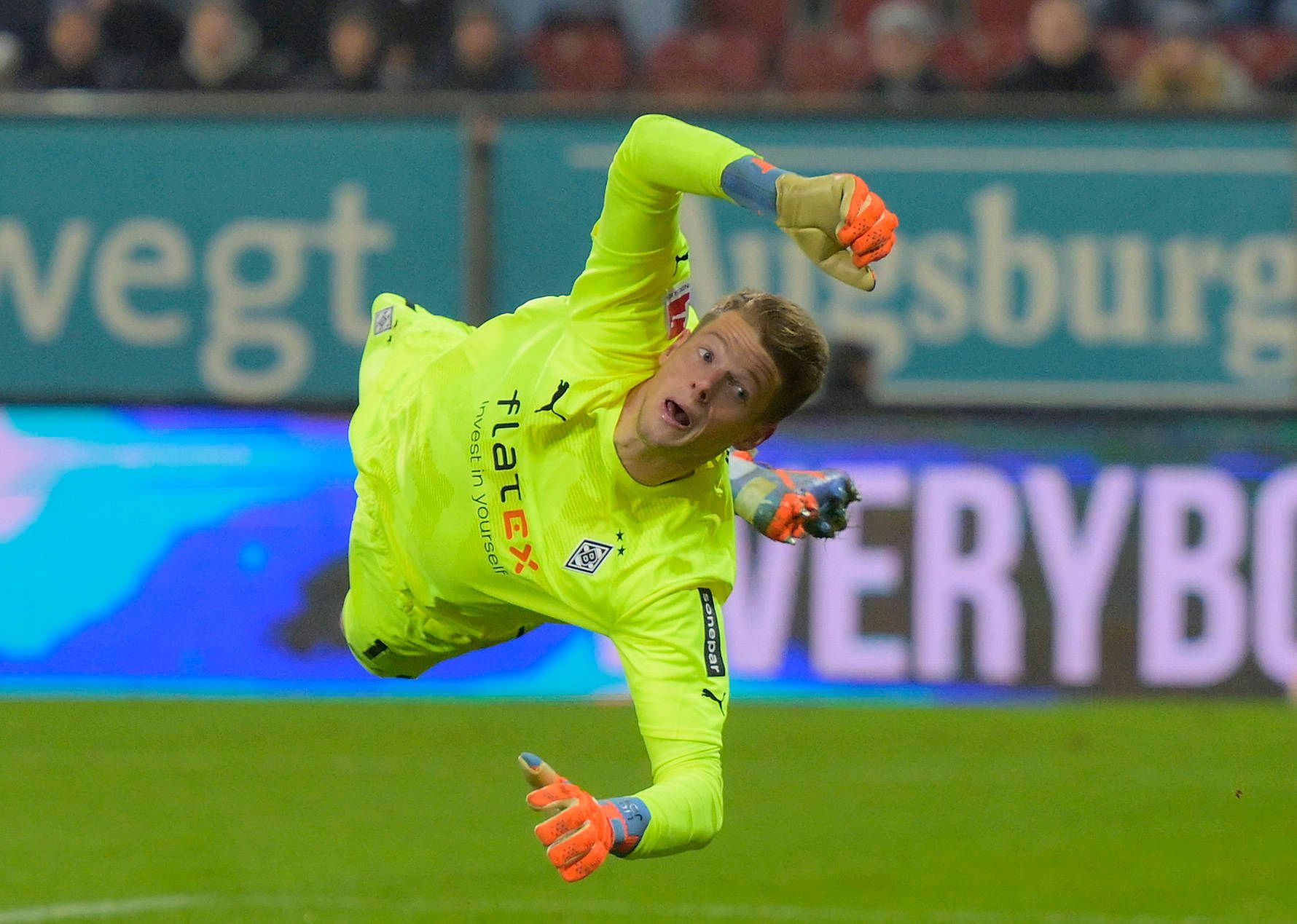 Jonas Omlin springt bei einer Parade im Bundesliga-Spiel von Borussia Mönchengladbach beim FC Augsburg am 25. Januar 2023 zur linken Seite. Omlin trägt ein knallgelbes Borussia-Trikot.