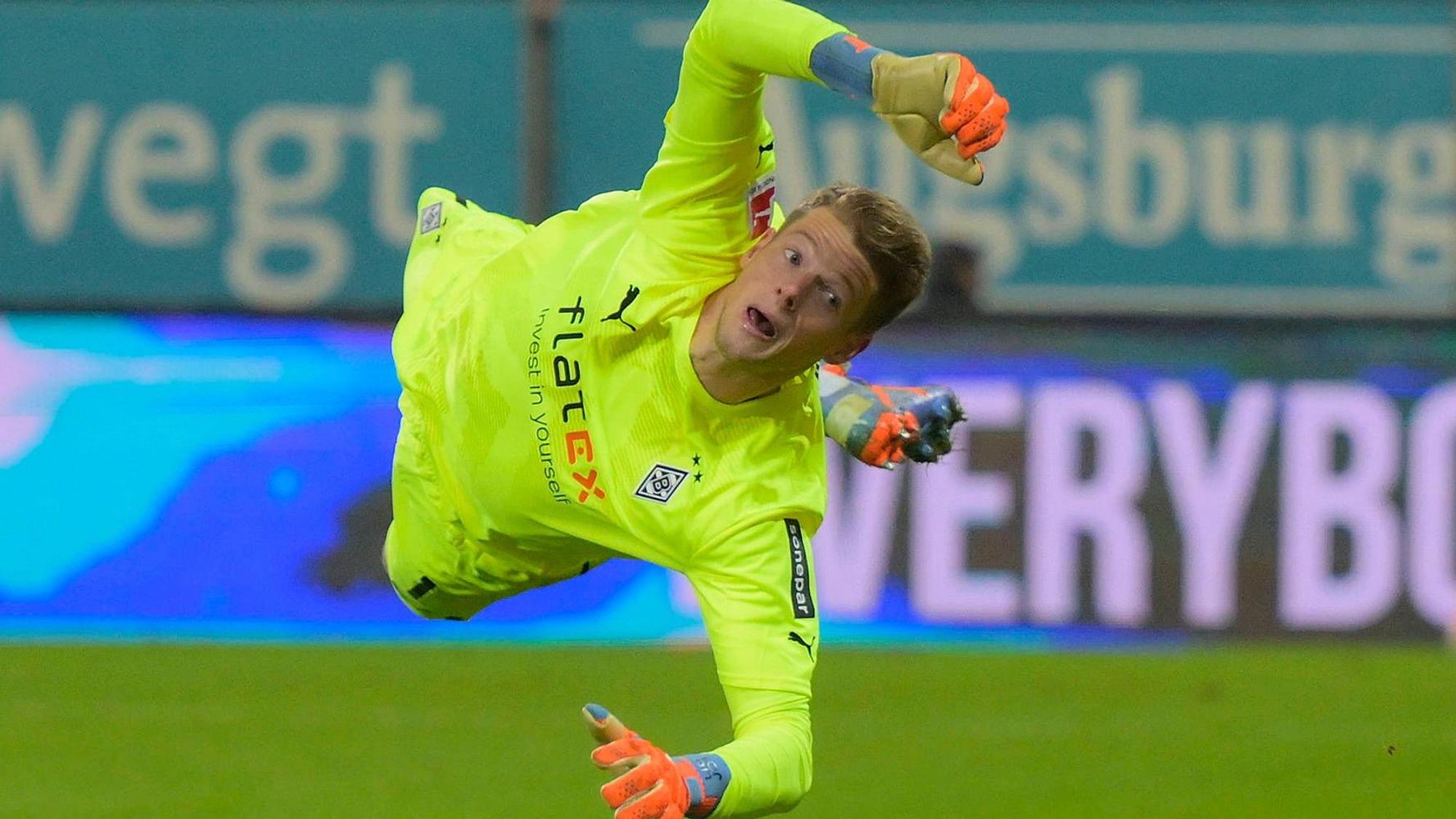 Jonas Omlin springt bei einer Parade im Bundesliga-Spiel von Borussia Mönchengladbach beim FC Augsburg am 25. Januar 2023 zur linken Seite. Omlin trägt ein knallgelbes Borussia-Trikot.