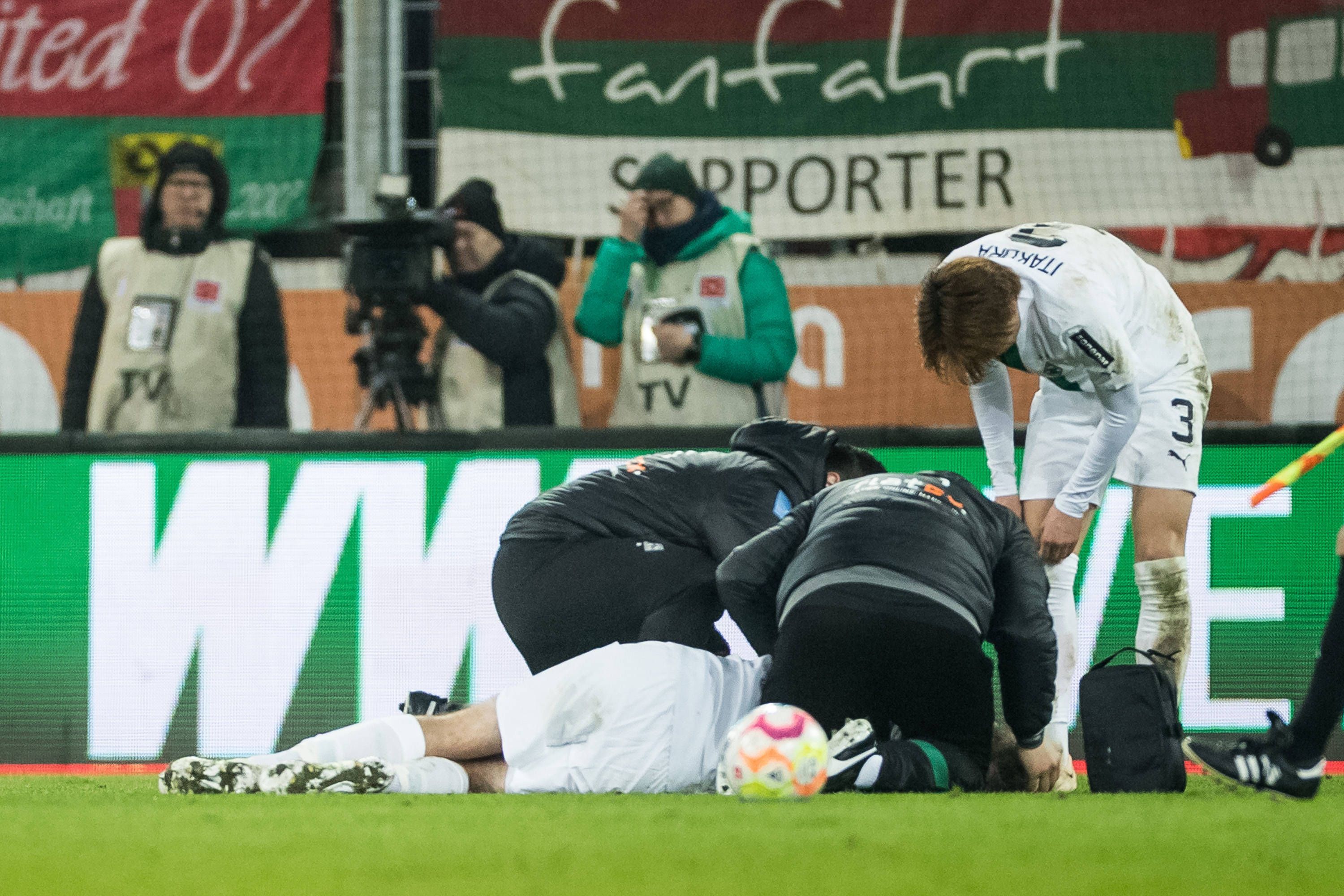 Christoph Kramer wird auf dem Rasen in der WWK-Arena in Augsburg behandelt. Die Mannschaftsärzte von Borussia Mönchengladbach und Mitspieler Ko Itakura stehen um ihn herum.