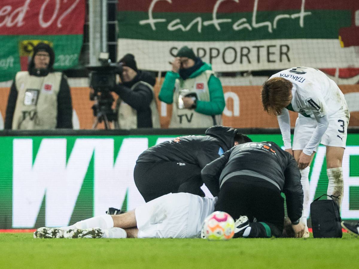 Christoph Kramer wird auf dem Rasen in der WWK-Arena in Augsburg behandelt. Die Mannschaftsärzte von Borussia Mönchengladbach und Mitspieler Ko Itakura stehen um ihn herum.