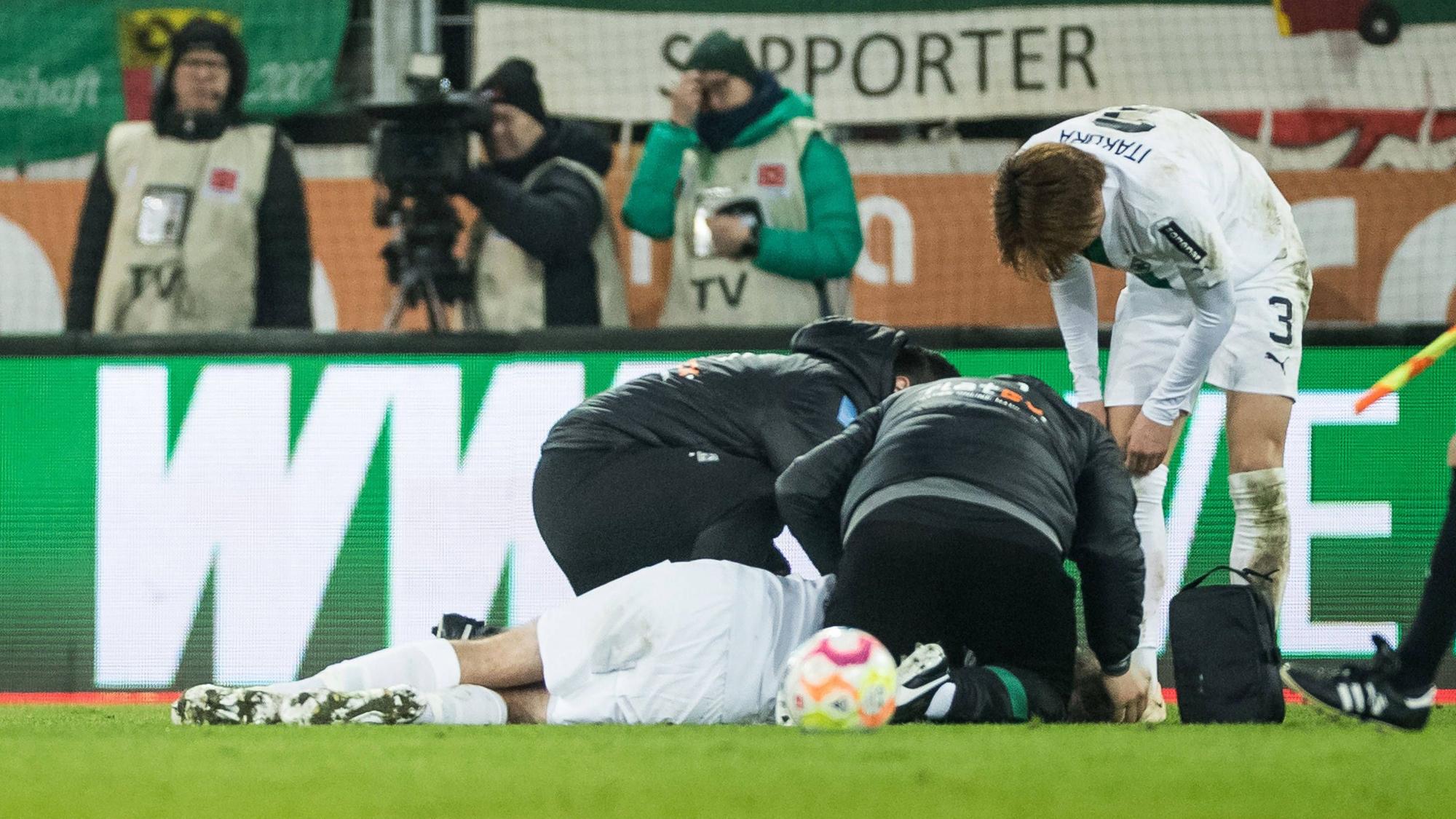 Christoph Kramer wird auf dem Rasen in der WWK-Arena in Augsburg behandelt. Die Mannschaftsärzte von Borussia Mönchengladbach und Mitspieler Ko Itakura stehen um ihn herum.