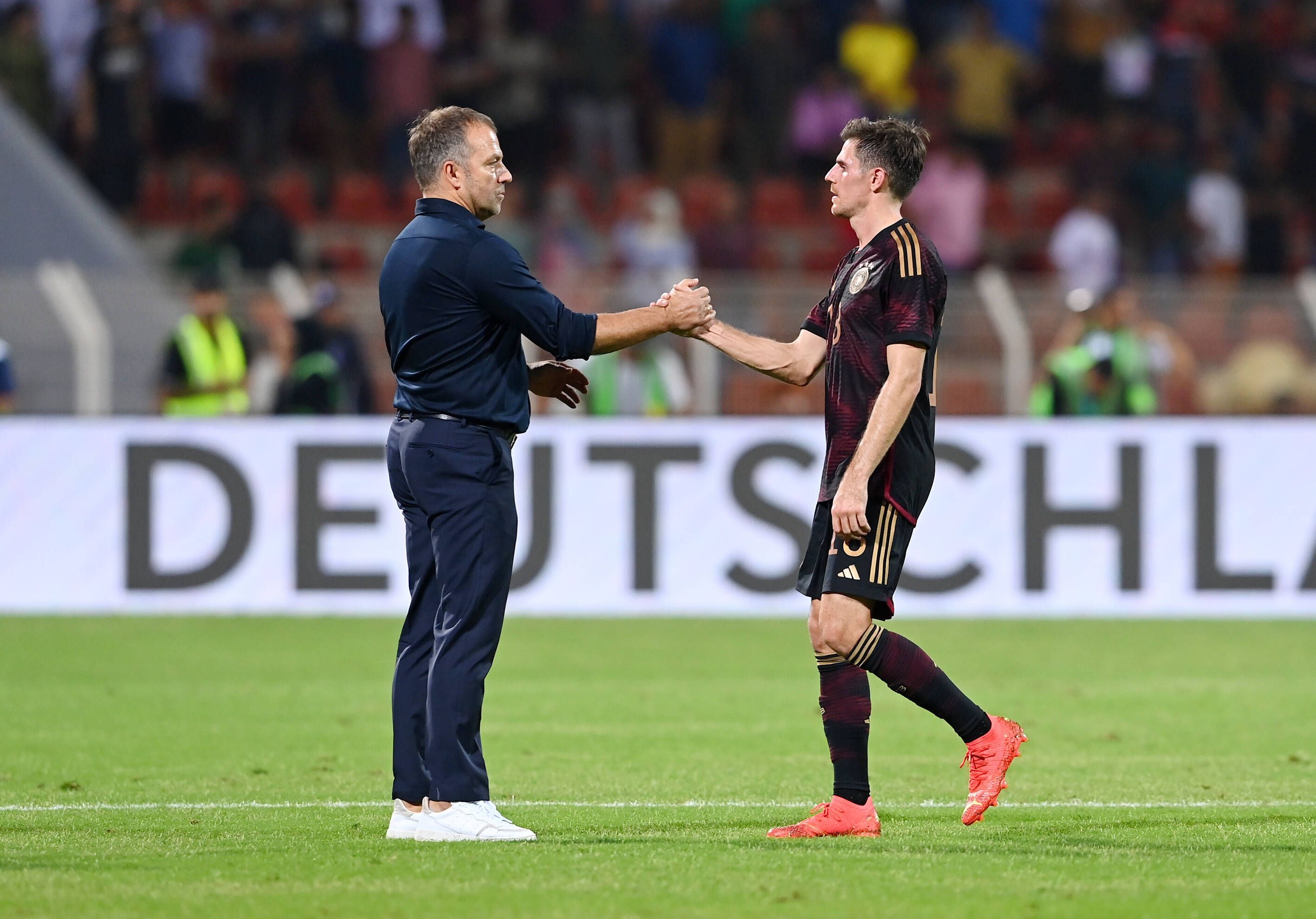 DFB-Bundestrainer Hansi Flick (l.) klatscht seinen Nationalspieler Jonas Hofmann (r.) ab. Dieses Foto zeigt die beiden am 16. November 2022 in Oman. Flick und Hofmann stehen auf dem Spielfeld.