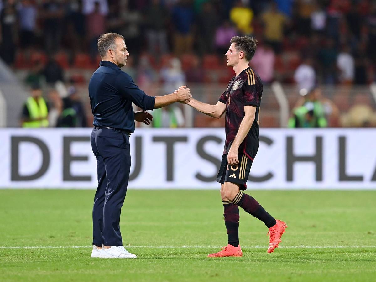 DFB-Bundestrainer Hansi Flick (l.) klatscht seinen Nationalspieler Jonas Hofmann (r.) ab. Dieses Foto zeigt die beiden am 16. November 2022 in Oman. Flick und Hofmann stehen auf dem Spielfeld.