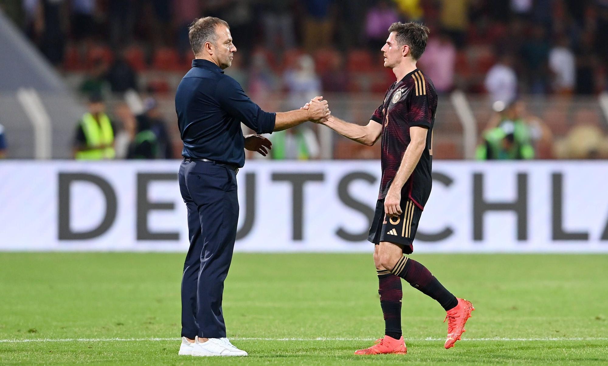 DFB-Bundestrainer Hansi Flick (l.) klatscht seinen Nationalspieler Jonas Hofmann (r.) ab. Dieses Foto zeigt die beiden am 16. November 2022 in Oman. Flick und Hofmann stehen auf dem Spielfeld.
