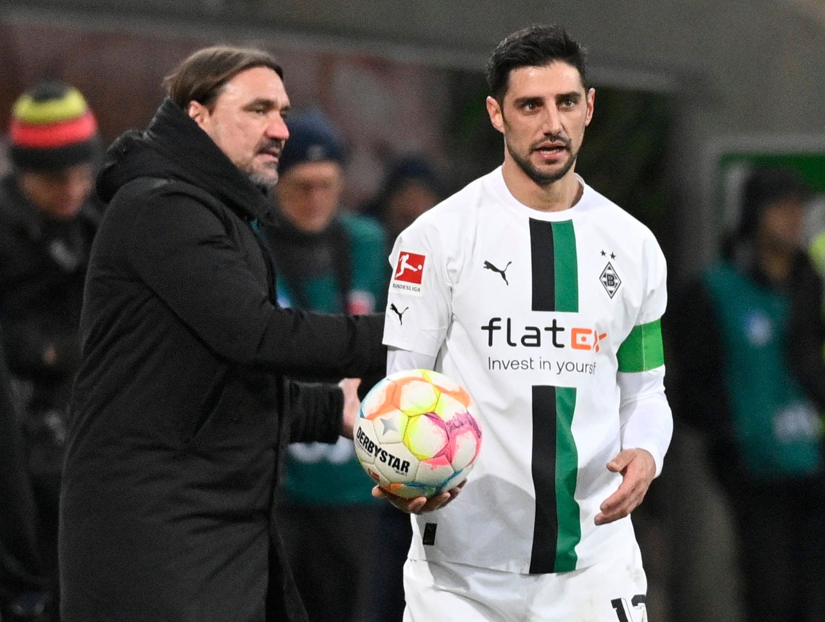 Daniel Farke (l.), Trainer von Borussia Mönchengladbach, gibt Kapitän Lars Stindl im Bundesliga-Spiel am 28. Januar 2023 bei der TSG Hoffenheim den Ball und spricht mit dem Gladbach-Spieler, der das weiße Heimtrikot von Borussia trägt.