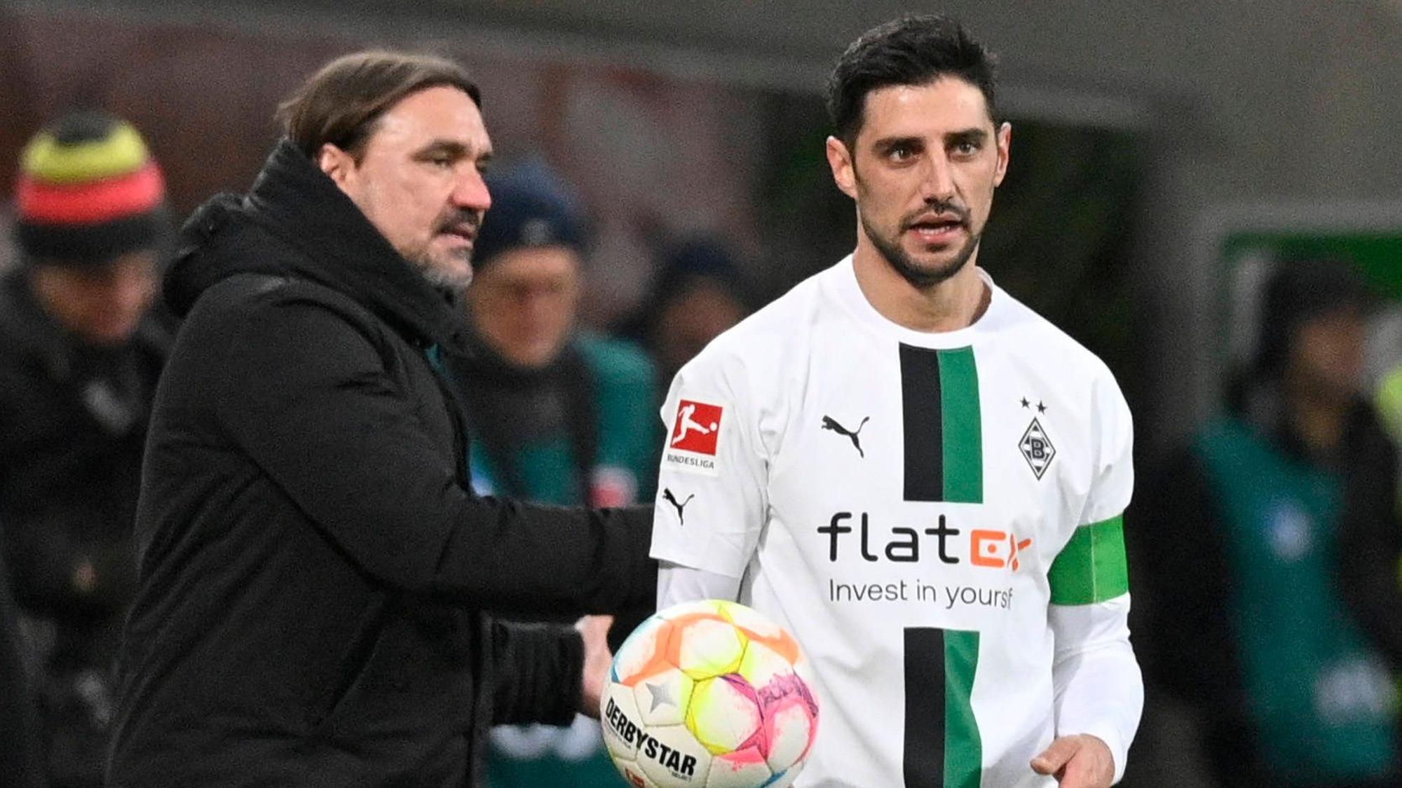 Daniel Farke (l.), Trainer von Borussia Mönchengladbach, gibt Kapitän Lars Stindl im Bundesliga-Spiel am 28. Januar 2023 bei der TSG Hoffenheim den Ball und spricht mit dem Gladbach-Spieler, der das weiße Heimtrikot von Borussia trägt.