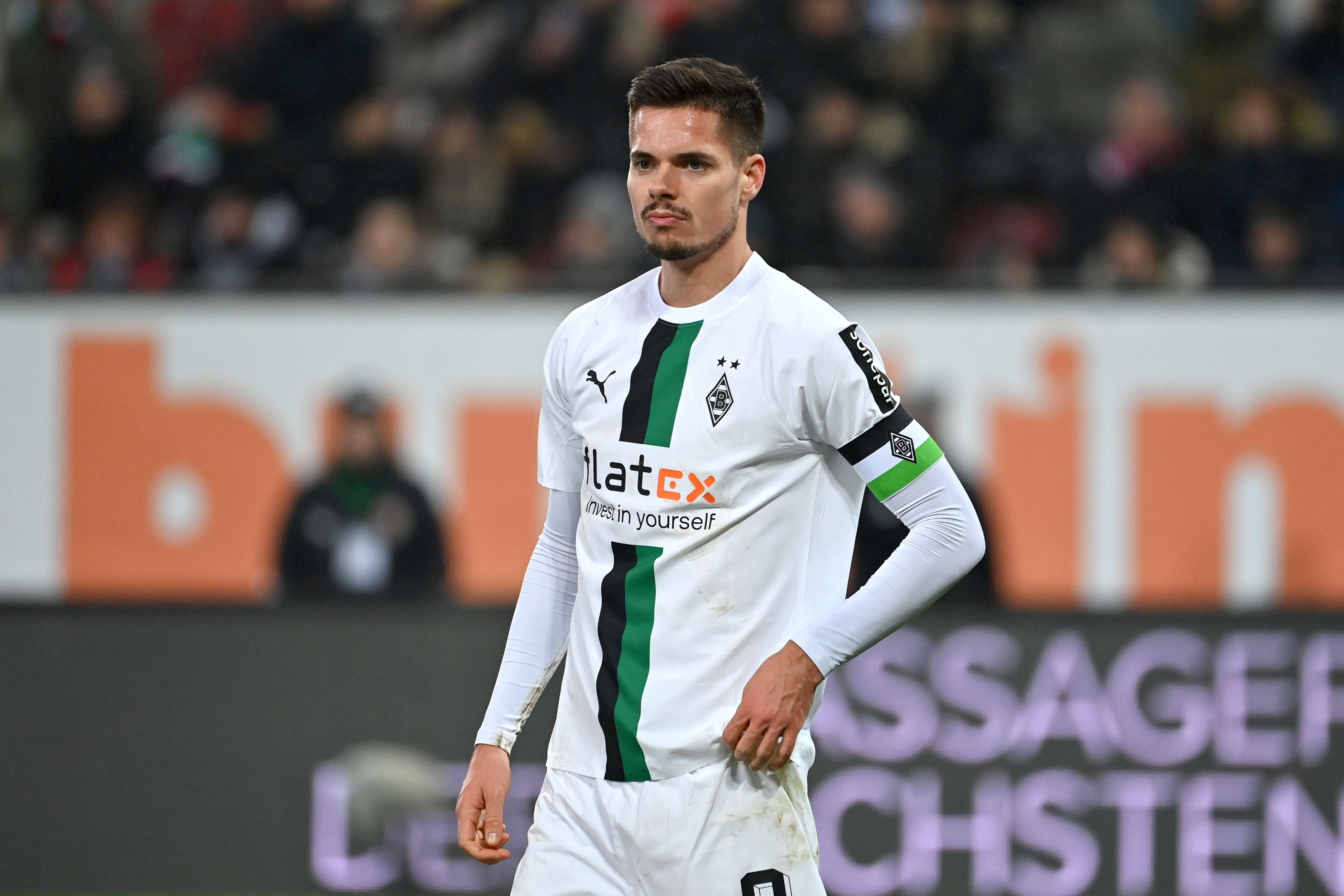DFB-Nationalspieler Julian Weigl hat sich bei Borussia Mönchengladbach in den Fokus gespielt, auf diesem Foto trägt die Leihgabe von Benfica Lissabon die Kapitänsbinde am 25. Januar 2023 in Augsburg. Weigl schaut nach vorne, er zupft an seinem Trikot rum.