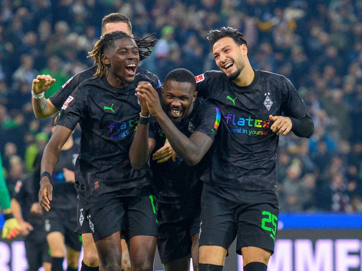 Manu Koné, Marcus Thuram und Ramy Bensebaini bejubeln einen Treffer von Borussia Mönchengladbach gegen Borussia Dortmund am 11. November 2022, feiern Arm in Arm und lachen. Das Gladbach-Trio trägt schwarze Trikots mit einem speziellen Regenbogen-Flock, das Trikot wurde nur beim BVB-Heimspiel am 15. Spieltag der Bundesliga-Saison getragen.