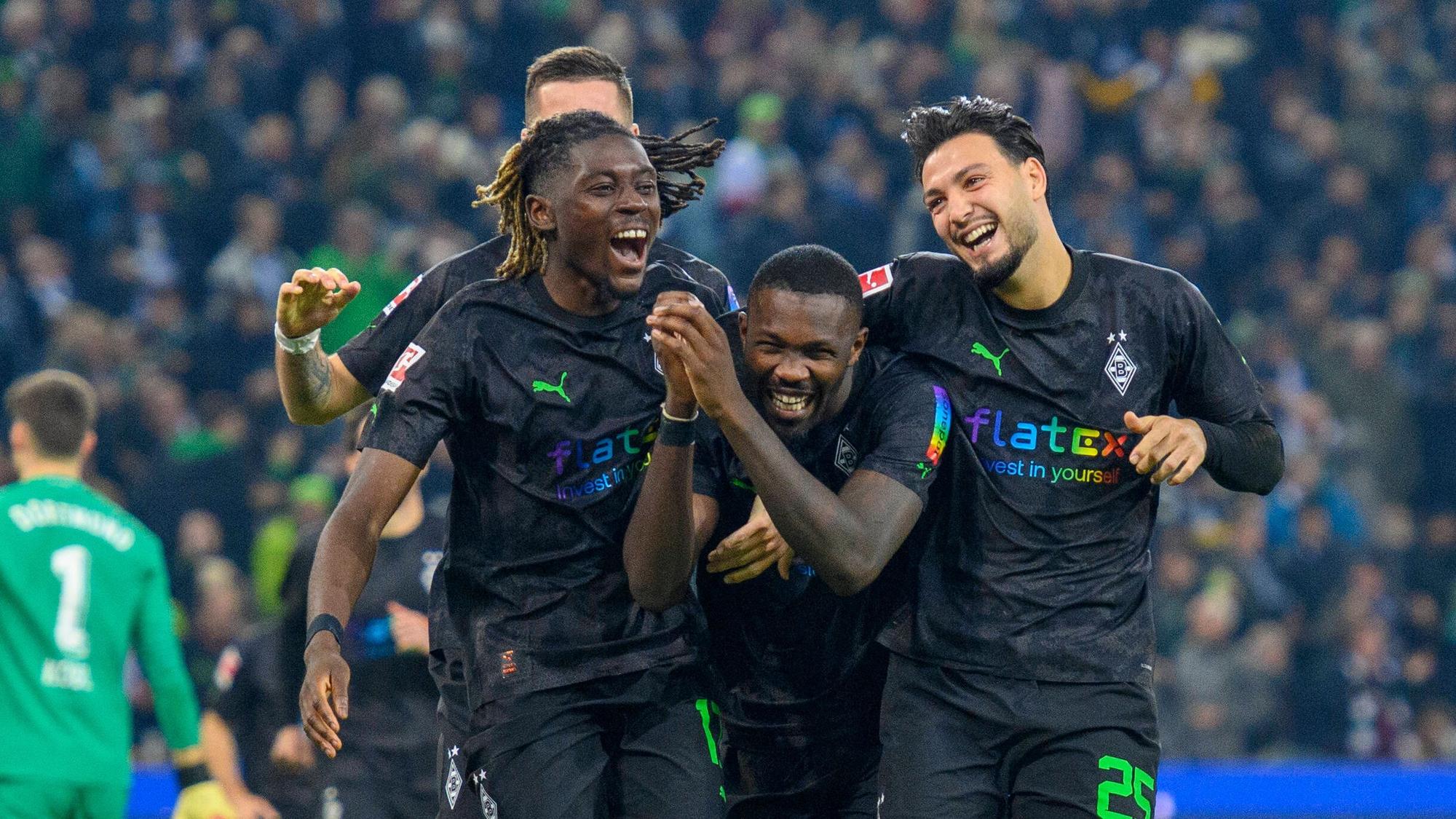Manu Koné, Marcus Thuram und Ramy Bensebaini bejubeln einen Treffer von Borussia Mönchengladbach gegen Borussia Dortmund am 11. November 2022, feiern Arm in Arm und lachen. Das Gladbach-Trio trägt schwarze Trikots mit einem speziellen Regenbogen-Flock, das Trikot wurde nur beim BVB-Heimspiel am 15. Spieltag der Bundesliga-Saison getragen.