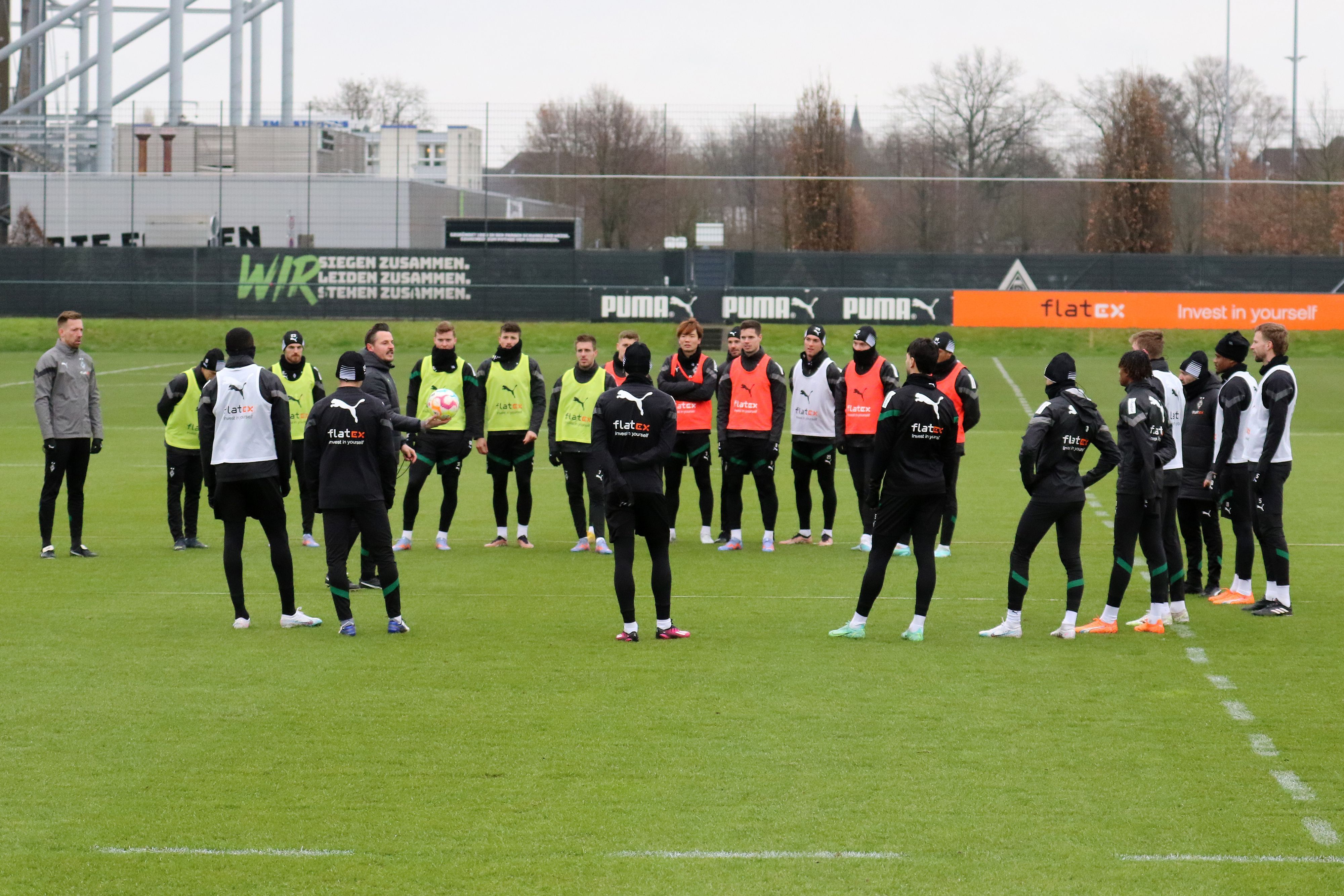 Das Team von Borussia Mönchengladbach steht bei einer Trainingseinheit am 2. Februar 2023 im Borussia-Park im Kreis zusammen. Co-Trainer Edmund Riemer gibt Anweisungen, einige Spieler tragen bunte Leibchen.