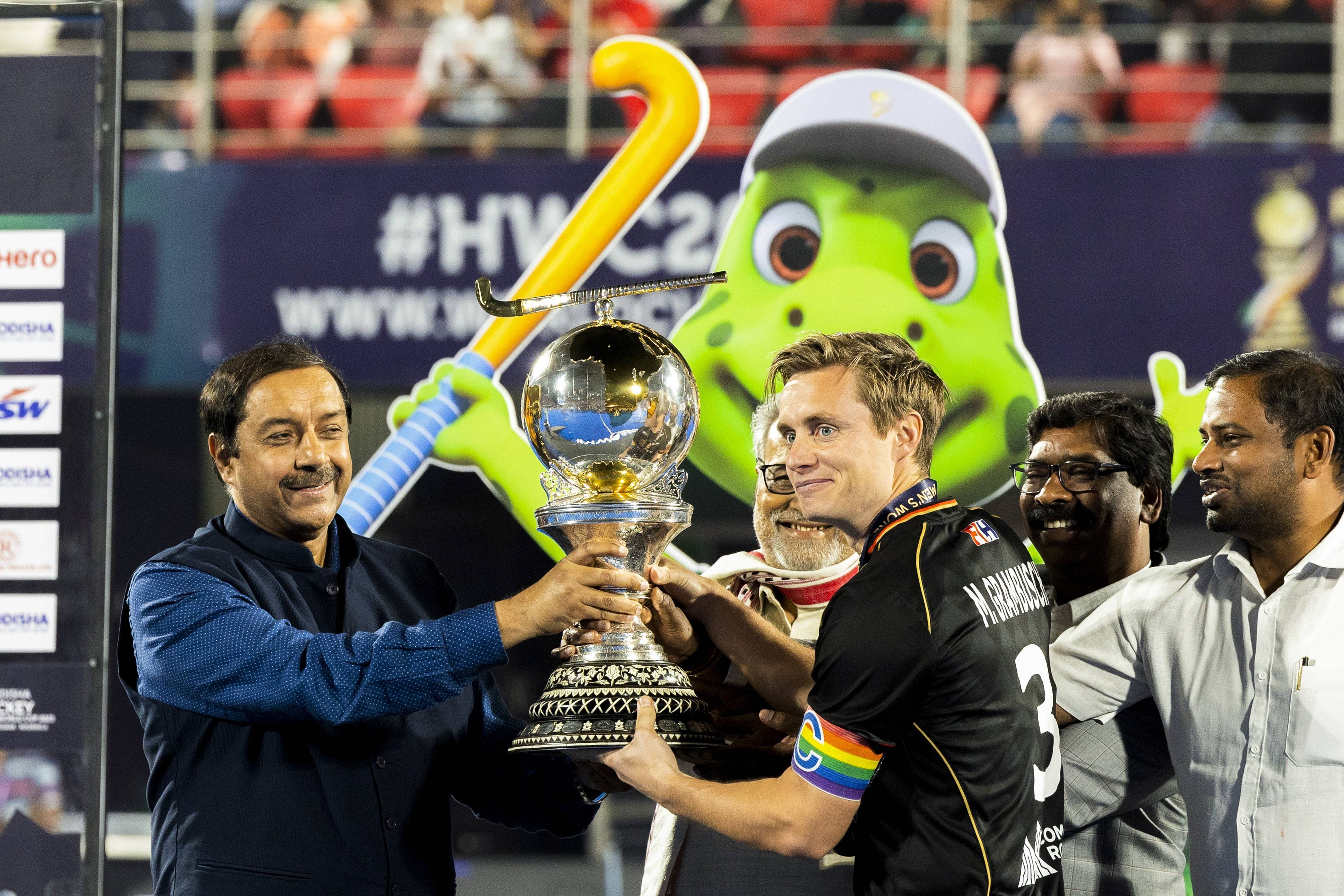 So sehen Weltmeister aus! Deutschland-Kapitän und Fohlen-Fan Mats Grambusch (r.) bekommt die Hockey-Trophäe am 29. Januar 2023 in Indien überreicht. Grambusch lächelt, er trägt eine Regenbogen-Armbinde.