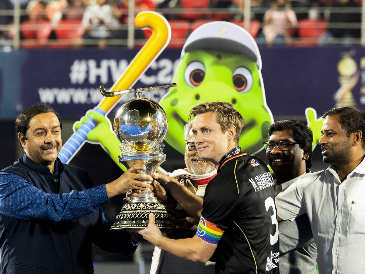 So sehen Weltmeister aus! Deutschland-Kapitän und Fohlen-Fan Mats Grambusch (r.) bekommt die Hockey-Trophäe am 29. Januar 2023 in Indien überreicht. Grambusch lächelt, er trägt eine Regenbogen-Armbinde.