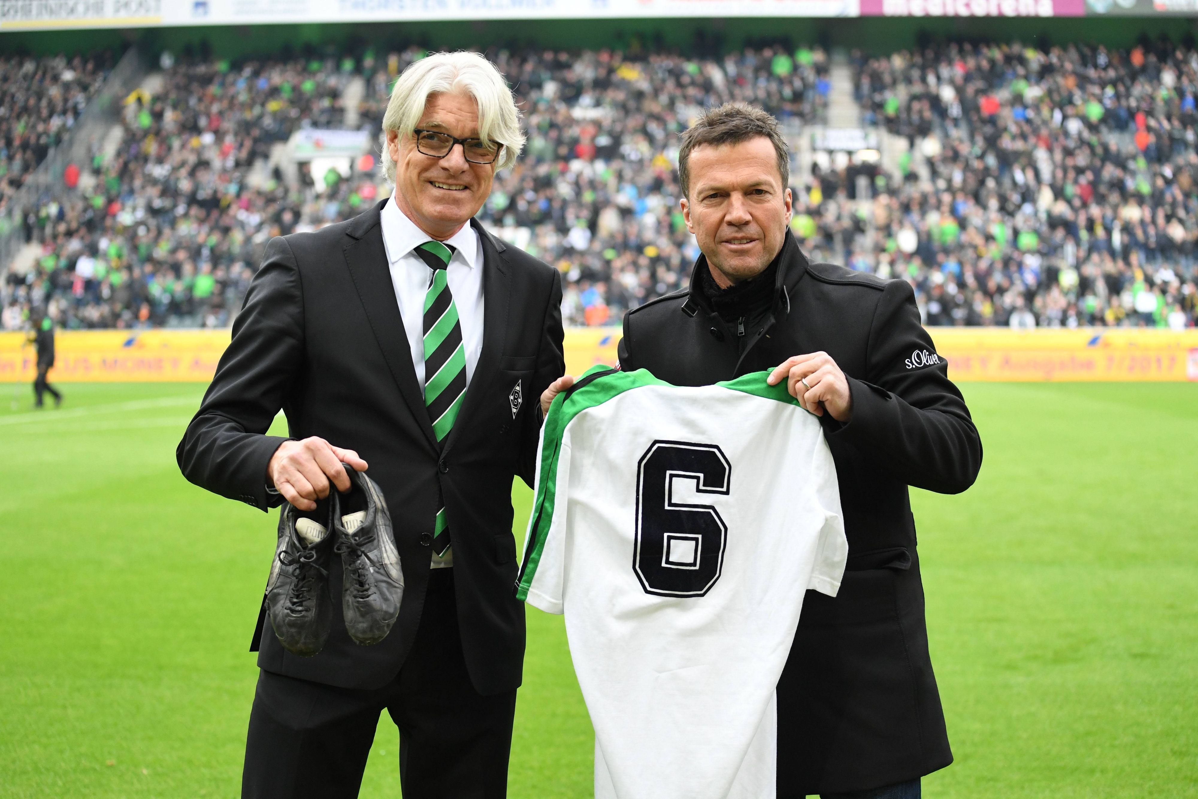 Der Mann für die Traditionspflege im Borussia-Park und der Weltmeister: Elmar Kreuels (l.) bekommt von Ex-Gladbach-Star Lothar Matthäus (r.) am 22. April 2017 dessen Original-Trikot aus alten Fohlen-Tagen samt Fußballschuhe überreicht. Beide lächeln in die Kamera. Matthäus zeigt sein Gladbach-Jersey, Kreuels hält die Schuhe in seiner rechten Hand.