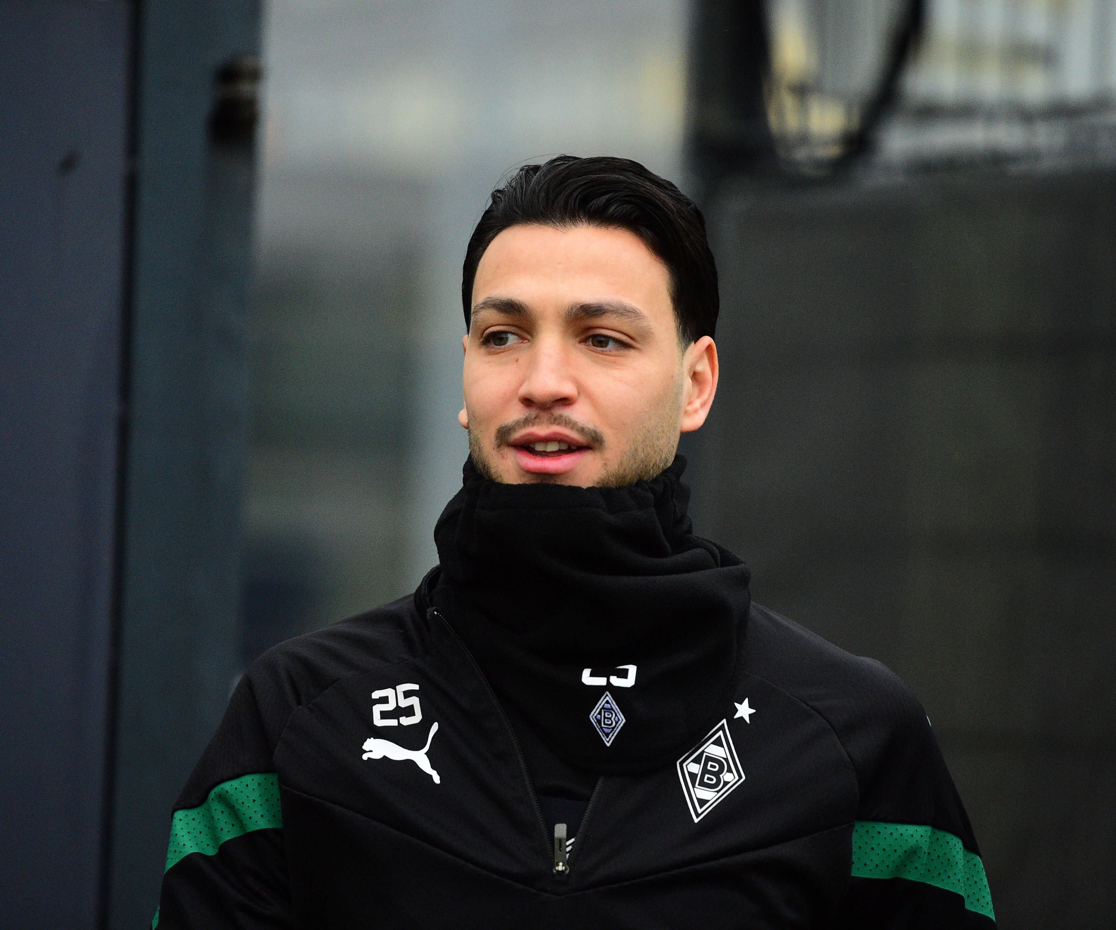 Ramy Bensebaini von Borussia Mönchengladbach, hier bei einer Trainingseinheit am 31. Januar 2023 in schwarze Kleidung und Schal eingepackt. Er lächelt bein Betreten des Platzes leicht.