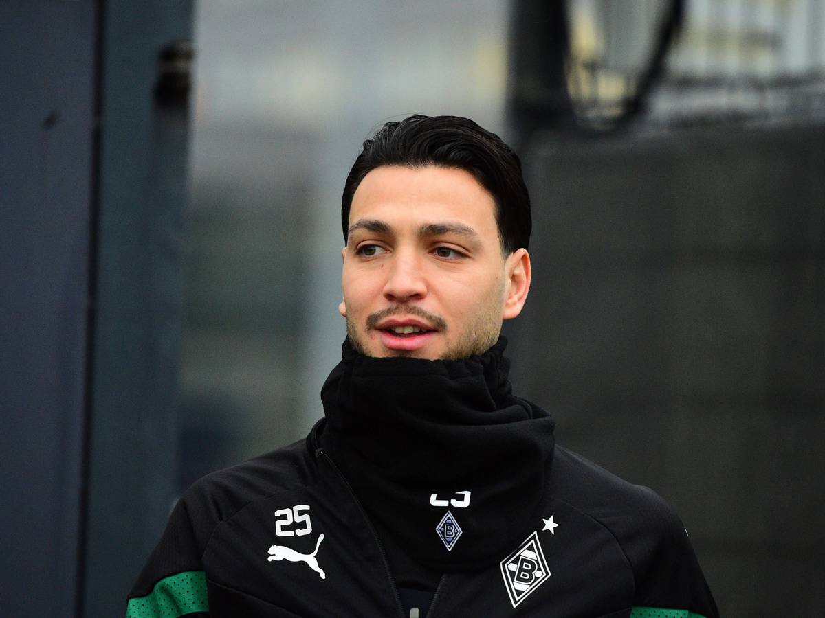 Ramy Bensebaini von Borussia Mönchengladbach, hier bei einer Trainingseinheit am 31. Januar 2023 in schwarze Kleidung und Schal eingepackt. Er lächelt bein Betreten des Platzes leicht.