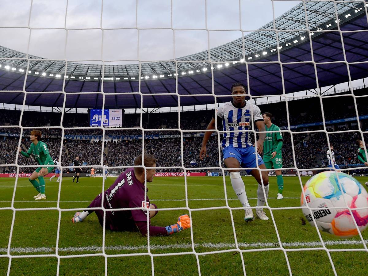 Jessic Ngankam (r.) schiebt den Ball zum zwischenzeitlichen 1:1-Ausgleich im Bundesliga-Spiel von Hertha BSC gegen Borussia Mönchengladbach ein. Jonas Omlin kann den Gegentreffer nicht mehr verhindern. Zu sehen ist, wie der Ball ins Netz des Borussia-Tores fliegt. Omlin springt vergeblich hinterher.