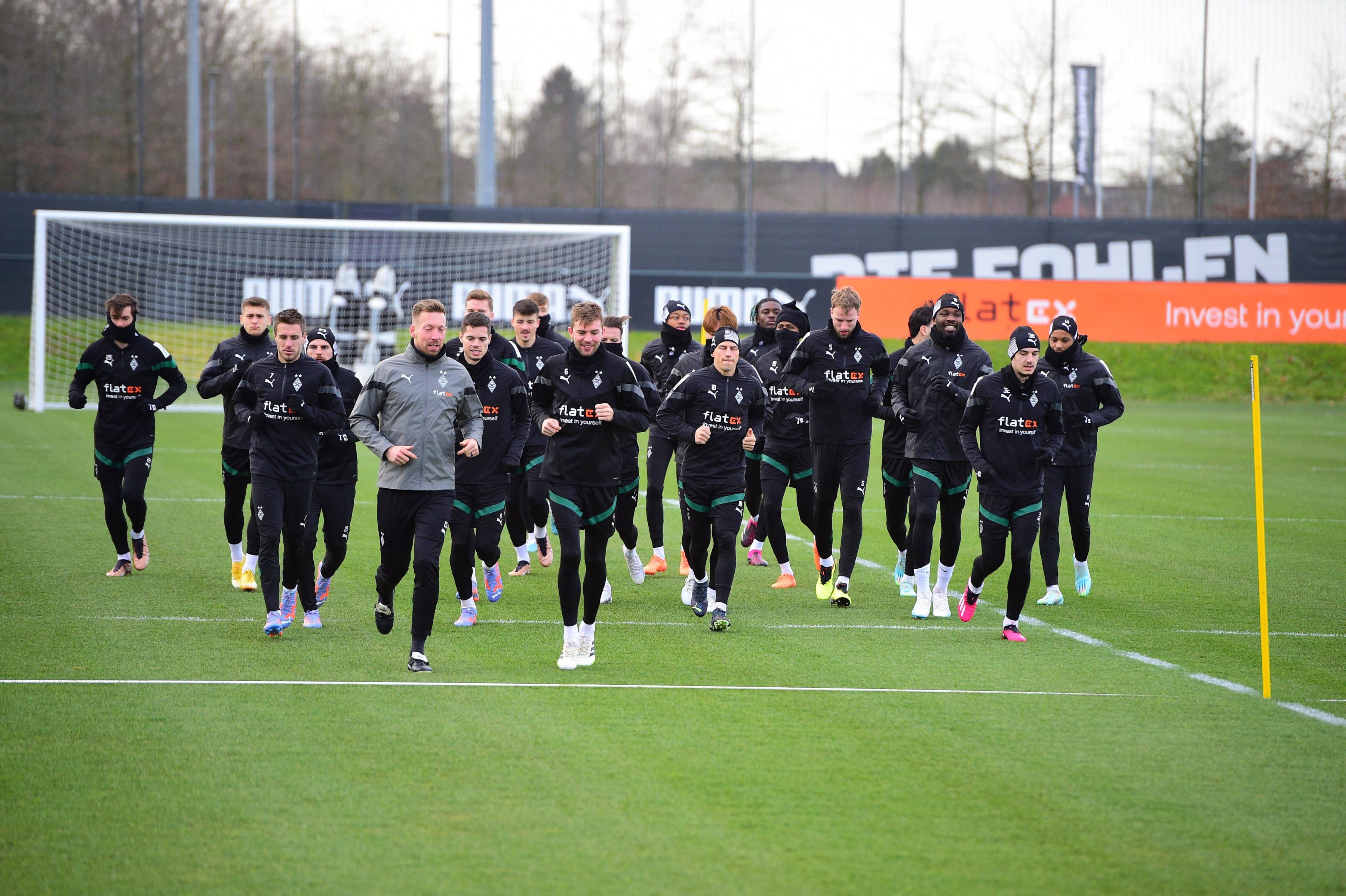 Die Spieler von Borussia Mönchengladbach laufen am 1. Februar 2023 gemeinschaftlich eine Runde auf dem Trainingsplatz-Rasen im Borussia-Park. Die Spieler tragen schwarze Gladbach-Trainingskleidung.