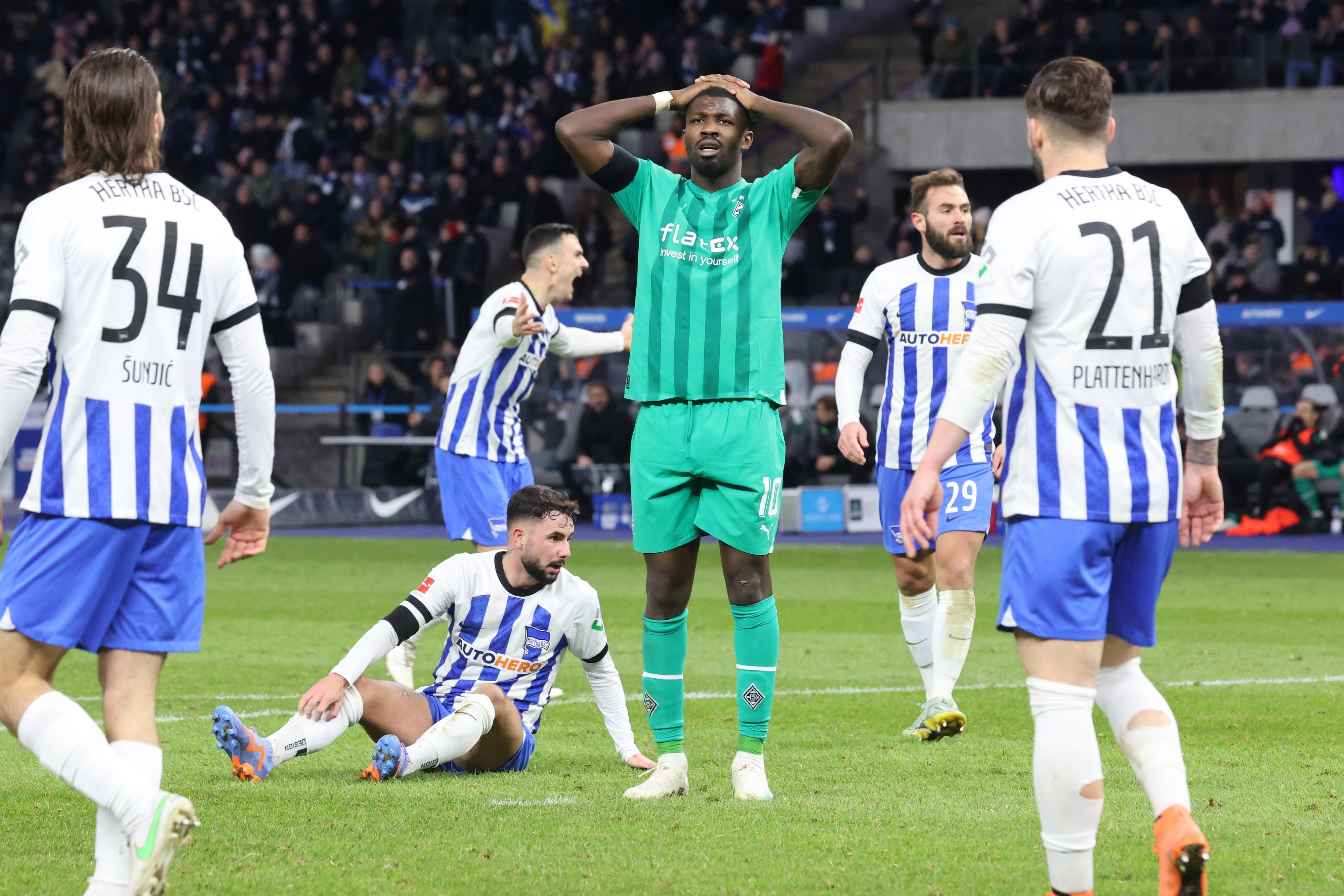 Marcus Thuram (in grün) von Borussia Mönchengladbach fasst sich nach einer vergebenen Torchance im Bundesliga-Spiel bei Hertha BSC mit den Händen an den Kopf. Bei dem Foto vom 12. Februar 2023 stehen fünf Spieler von Hertha BSC um den Gladbach-Stürmer herum.