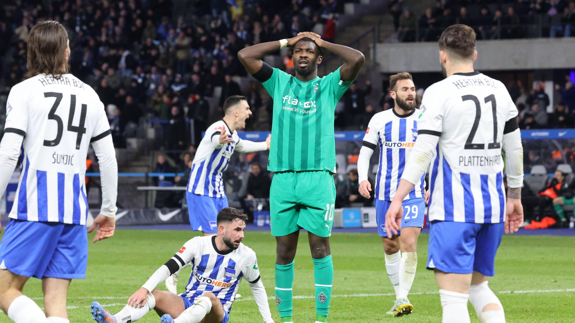 Marcus Thuram (in grün) von Borussia Mönchengladbach fasst sich nach einer vergebenen Torchance im Bundesliga-Spiel bei Hertha BSC mit den Händen an den Kopf. Bei dem Foto vom 12. Februar 2023 stehen fünf Spieler von Hertha BSC um den Gladbach-Stürmer herum.