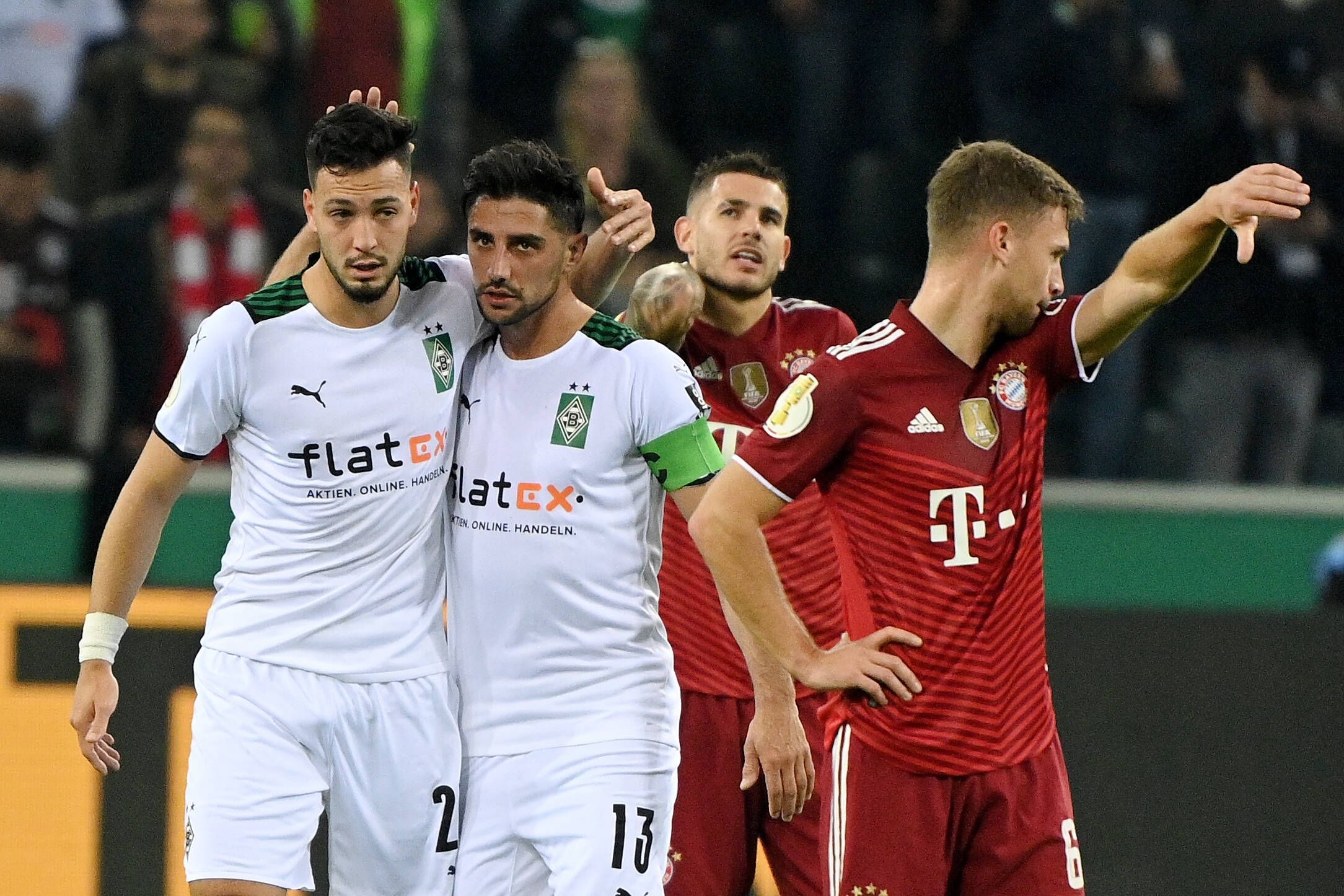 Ramy Bensebaini (l.) und Lars Stindl (2.v.l.), Spieler von Borussia Mönchengladbach, bejubeln gemeinsam einen Treffer im Spiel gegen den FC Bayern München am 27. Oktober 2021 im Borussia-Park. Stindl und Bensebaini liegen sich in den Armen. Die Bayern-Spieler Lucas Hernandez (2.v.r.) und Joshua Kimmich (r.) schauen enttäuscht drein.