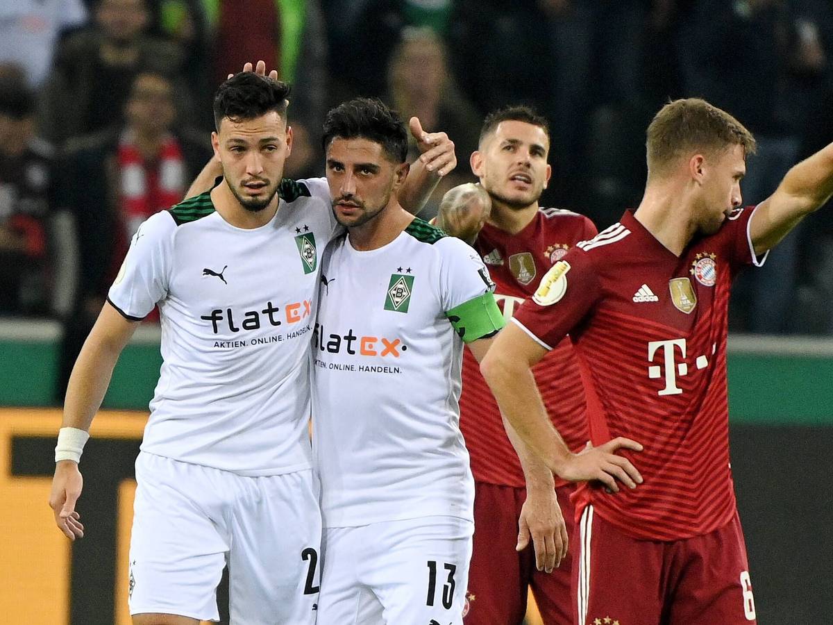 Ramy Bensebaini (l.) und Lars Stindl (2.v.l.), Spieler von Borussia Mönchengladbach, bejubeln gemeinsam einen Treffer im Spiel gegen den FC Bayern München am 27. Oktober 2021 im Borussia-Park. Stindl und Bensebaini liegen sich in den Armen. Die Bayern-Spieler Lucas Hernandez (2.v.r.) und Joshua Kimmich (r.) schauen enttäuscht drein.