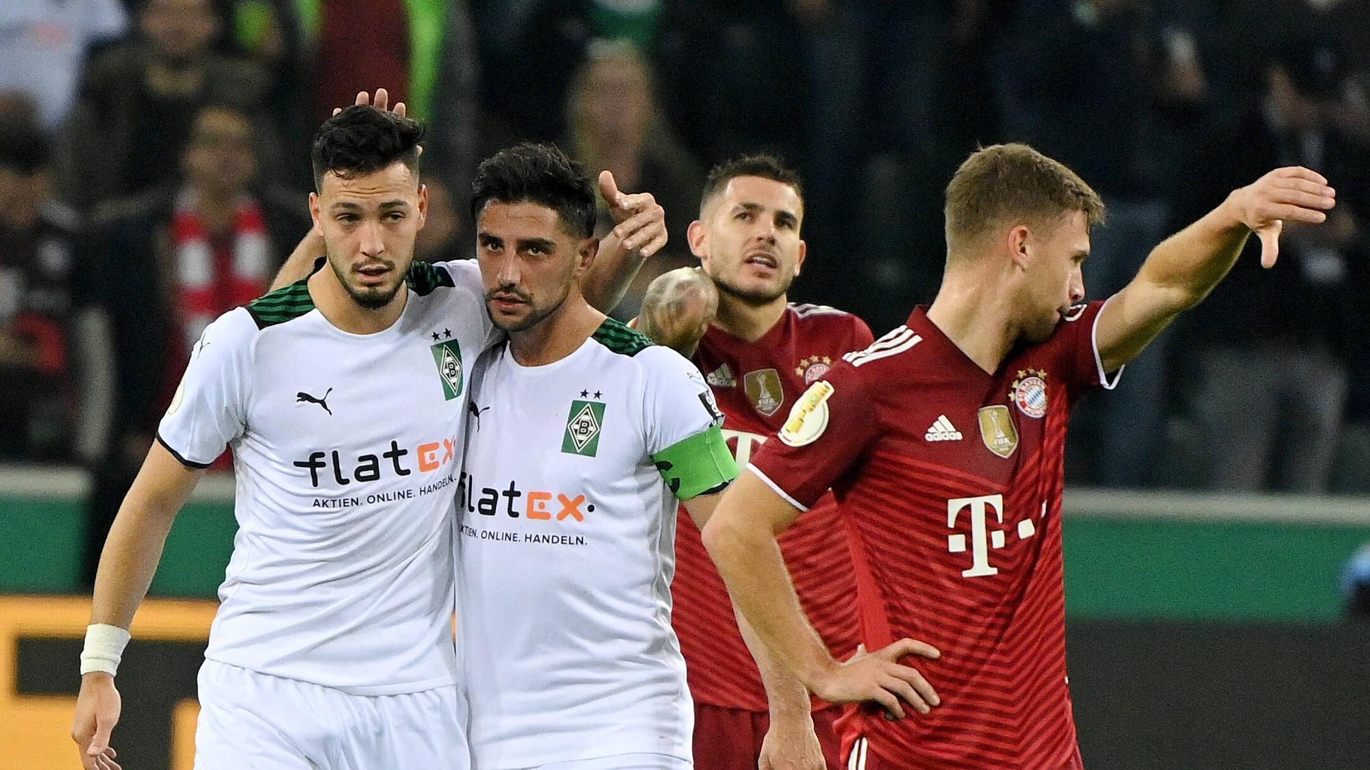 Ramy Bensebaini (l.) und Lars Stindl (2.v.l.), Spieler von Borussia Mönchengladbach, bejubeln gemeinsam einen Treffer im Spiel gegen den FC Bayern München am 27. Oktober 2021 im Borussia-Park. Stindl und Bensebaini liegen sich in den Armen. Die Bayern-Spieler Lucas Hernandez (2.v.r.) und Joshua Kimmich (r.) schauen enttäuscht drein.