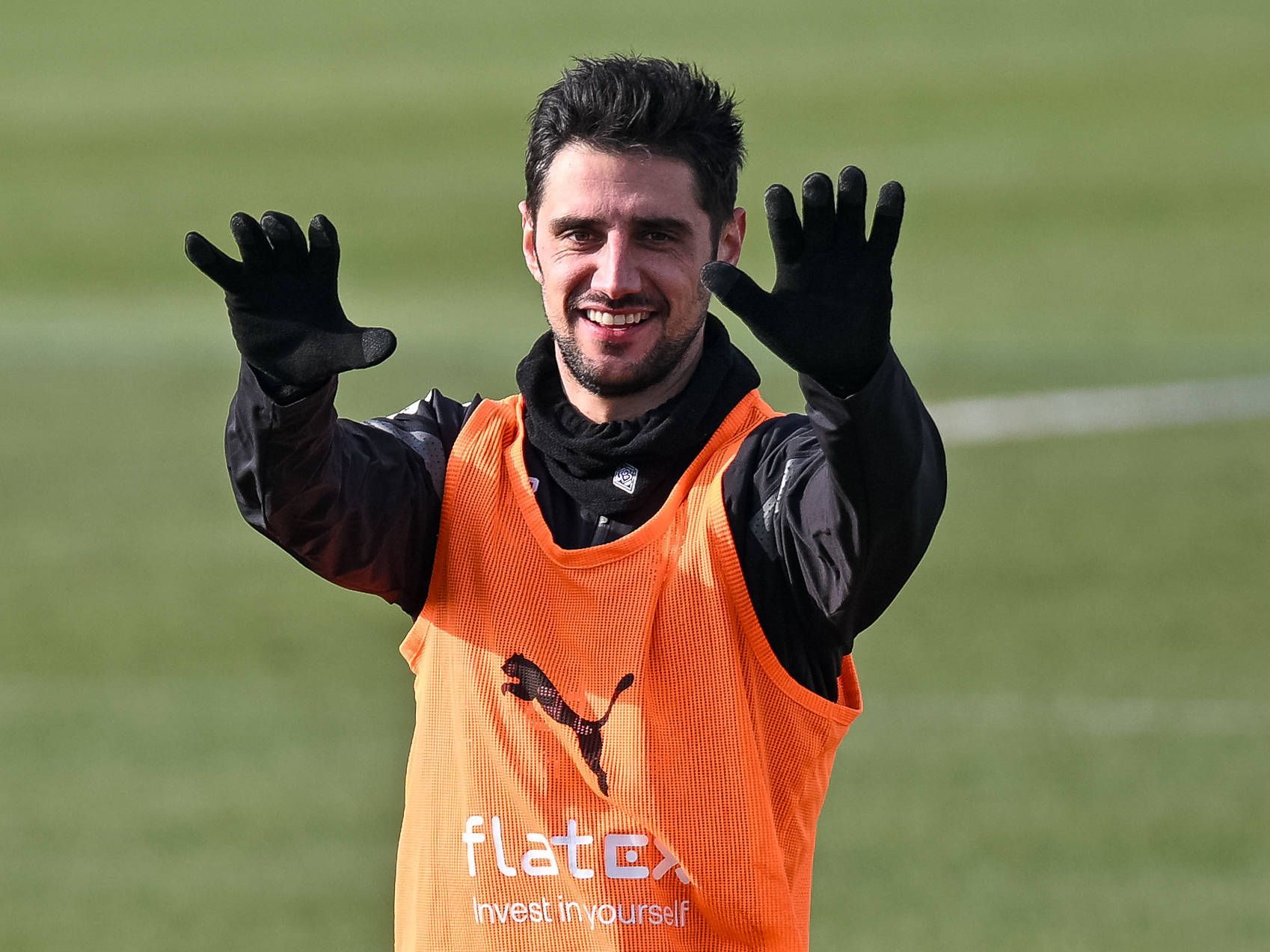 Lars Stindl streckt im Training von Borussia Mönchengladbach beide Arme nach vorne und lächelt. Der Gladbach-Kapitän trägt bei der Einheit auf dem Trainingsplatz im Borussia-Park am 9. Februar 2023 dunkle Trainingskleidung und ein Leibchen.