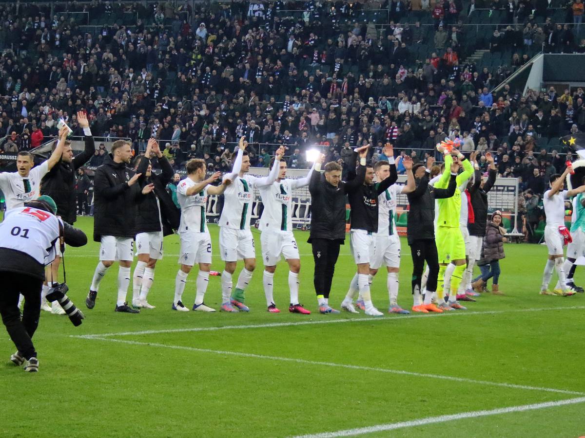 Die Mannschaft von Borussia Mönchengladbach feiert nach dem 3:2-Heimsieg gegen den FC Bayern München am 18. Februar 2023 mit den Fans im Borussia-Park. Die Spieler halten sich an den Händen und machen die La-Ola-Welle vor der Nordkurve.