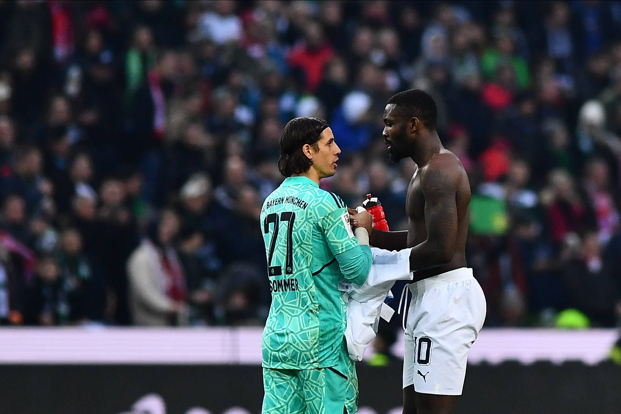 Ex-Gladbach-Torwart Yann Sommer (l.) klatscht sich nach der Bundesliga-Niederlage seines neuen Klubs Bayern München mit Borussia-Stürmer Marcus Thuram (r.) ab. Thuram hat einen nackten Oberkörper und möchte das Trikot mit Sommer tauschen.