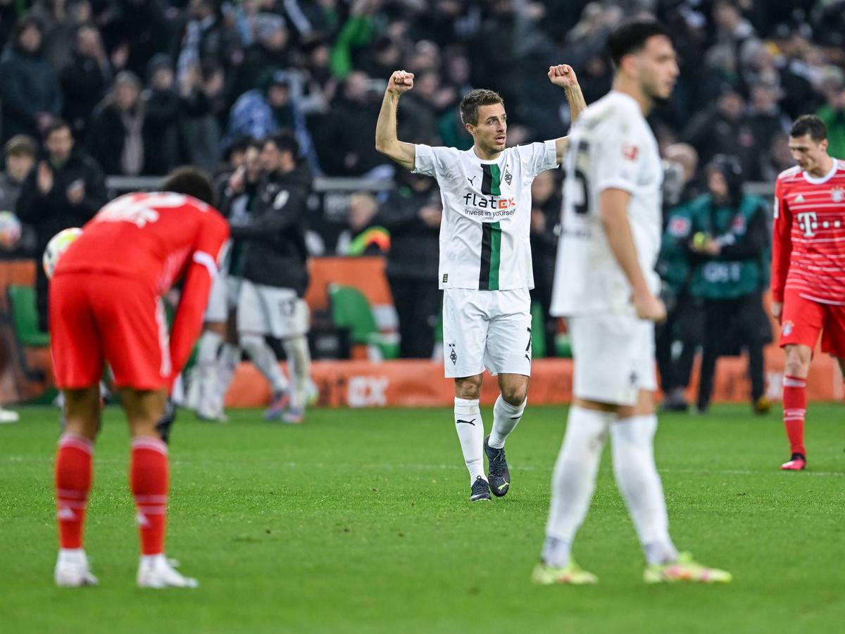 Patrick Herrmann reißt nach dem Schlusspfiff des Bundesliga-Spiels von Borussia Mönchengladbach gegen den FC Bayern München am 18. Februar 2023 die Arme nach oben. In der Nähe von Herrmann stehen die Bayern-Profis und Teamkollege Ramy Bensebaini. Herrmann trägt das weiße Gladbach-Heimtrikot.