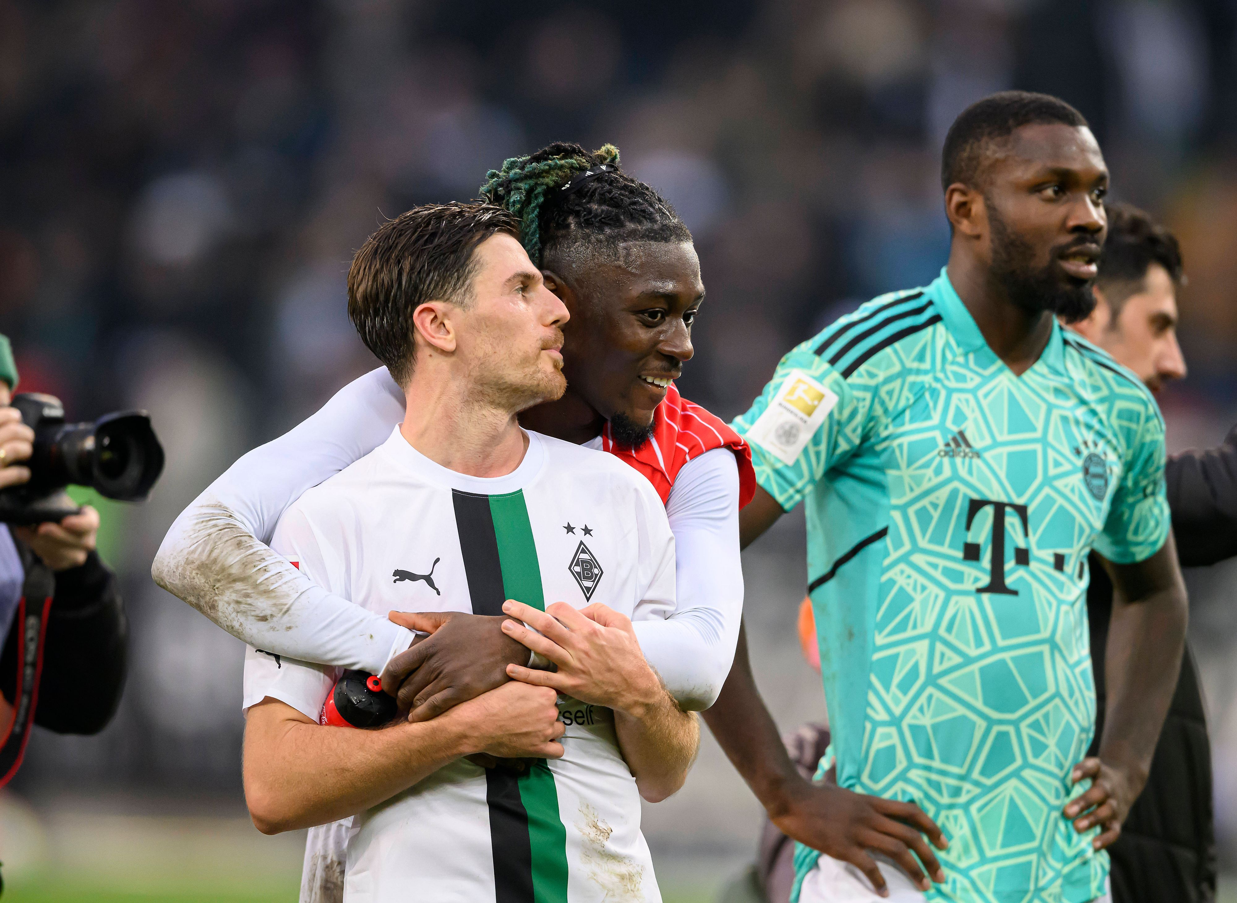 Manu Koné steht nach dem Bundesliga-Sieg von Borussia Mönchengladbach gegen den FC Bayern München am 18. Februar 2023 hinter seinem Teamkollegen Jonas Hofmann und legt seine Arme freundschaftlich um ihn. Marcus Thuram (r.) steht im Bayern-Trikot von Yann Sommer neben dem Gladbach-Duo auf dem Rasen im Borussia-Park.
