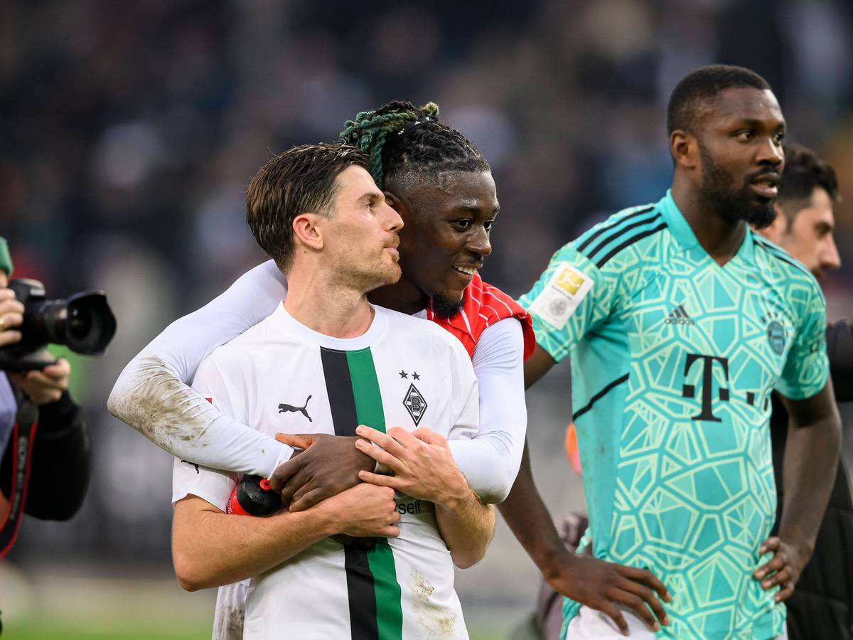 Manu Koné steht nach dem Bundesliga-Sieg von Borussia Mönchengladbach gegen den FC Bayern München am 18. Februar 2023 hinter seinem Teamkollegen Jonas Hofmann und legt seine Arme freundschaftlich um ihn. Marcus Thuram (r.) steht im Bayern-Trikot von Yann Sommer neben dem Gladbach-Duo auf dem Rasen im Borussia-Park.
