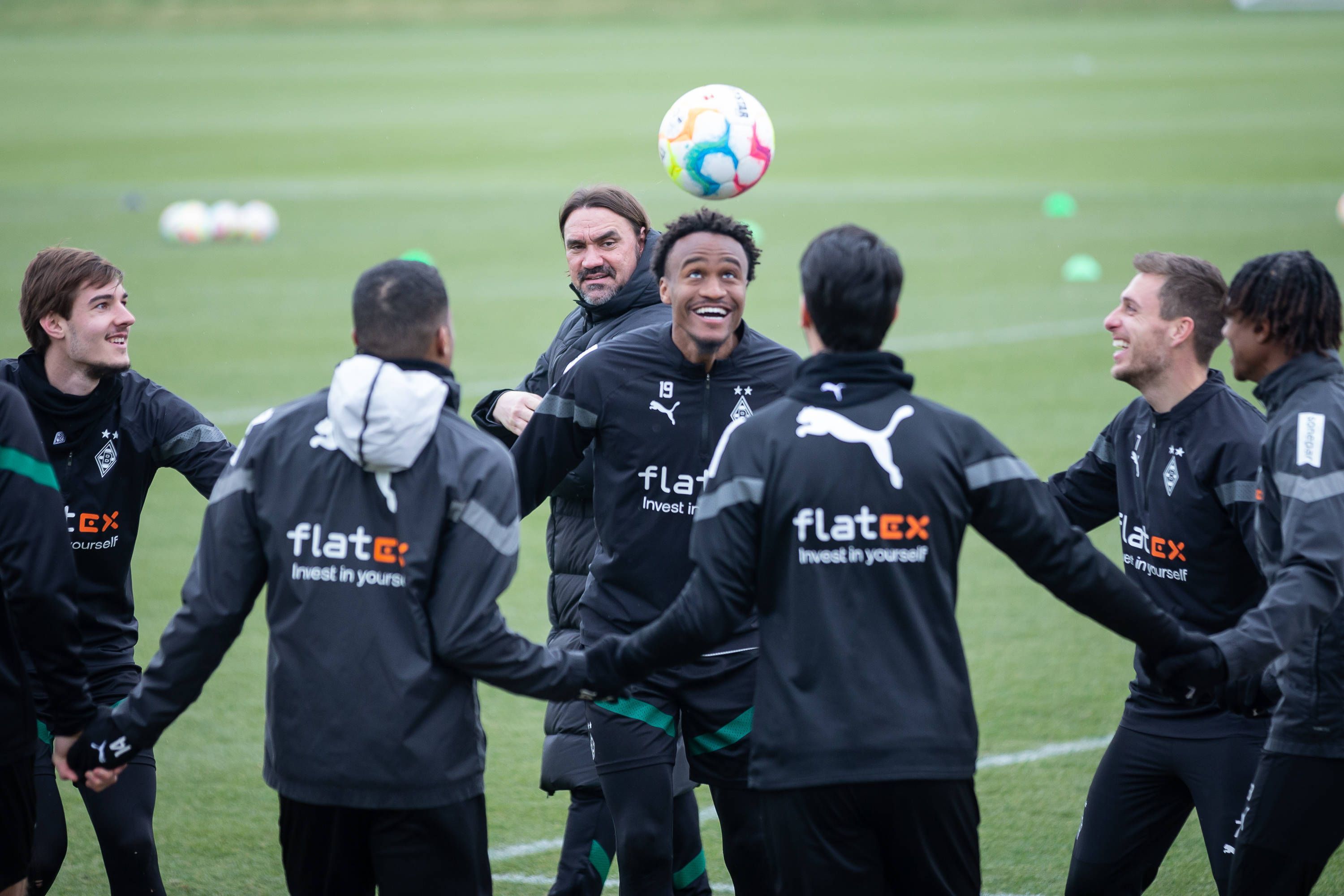 Ein bisschen Spaß muss sein! Gute Laune bei Borussia nach dem Heim-Coup gegen Bayern München. Die Gladbach-Profis, hier zu sehen am 16. Februar im Borussia-Park, beginnen nun mit der Vorbereitung auf das Mainz-Spiel. Zu sehen ist Ngoumou beim Kopfball, der Franzose lächelt, er hält seinen Team-Kollegen, die einen Kreis gebildet haben, an den Händen. Im Hintergrund schaut Trainer Daniel Farke zu.