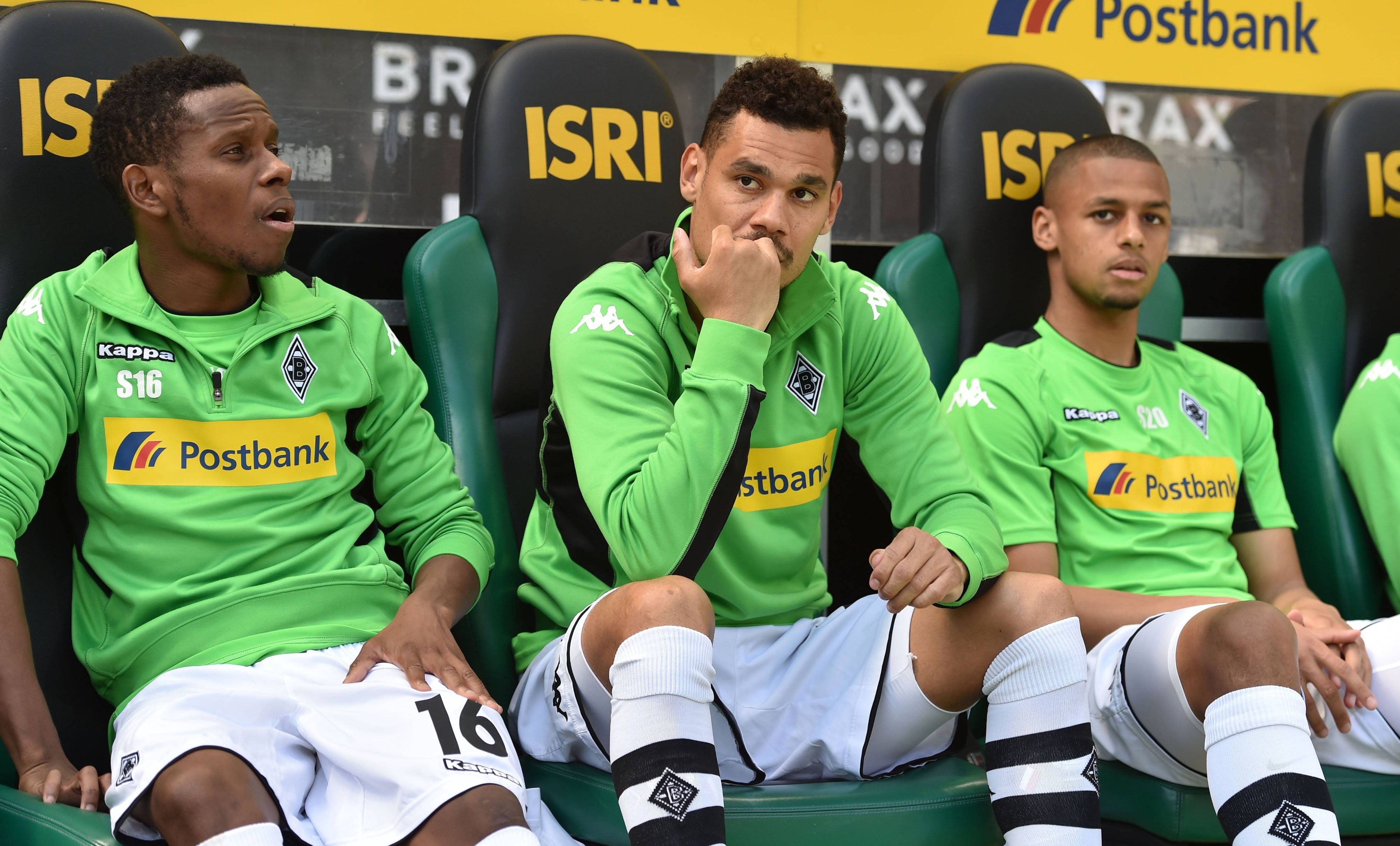 Timothee Kolodziejczak (M.) sitzt am 6. Mai 2017 auf der Ersatzbank von Borussia Mönchengladbach im Borussia-Park zwischen seinen damaligen Teamkollegen Ibrahima Traoré (l.) und Djibril Sow. Alle tragen ein grünes Trainings-Oberteil sowie weiße Hosen und Stutzen.