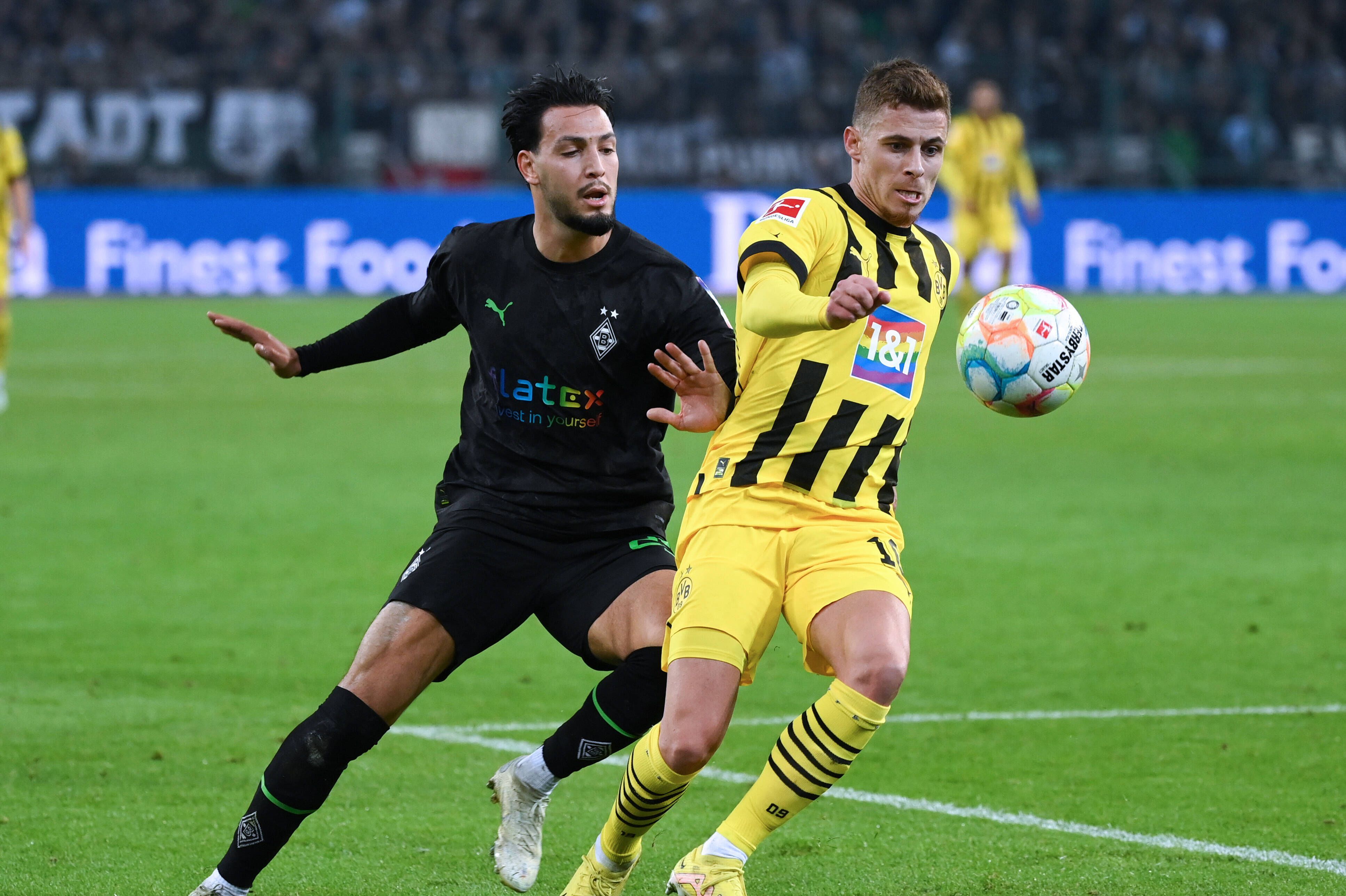 Ramy Bensebaini (l.) von Borussia Mönchengladbach im Duell mit Ex-Dortmund-Profi Thorgan Hazard (r.). Hier zu sehen im Bundesliga-Hinrunden-Match am 11. November 2022. Beide Spieler haben den Ball im Blick.